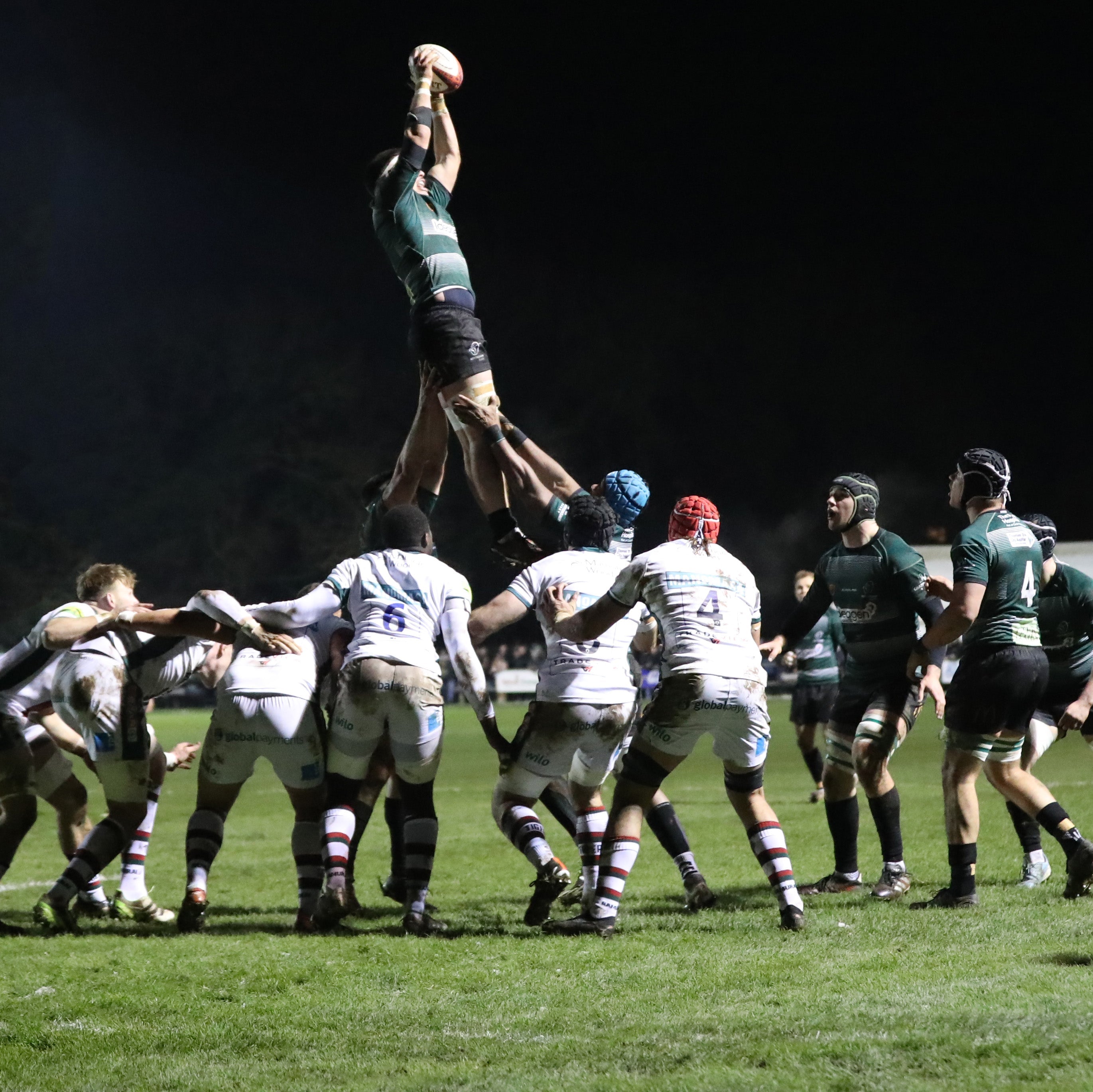 A group of Nottingham Rugby players play a game of Rugby on a pitch at night.