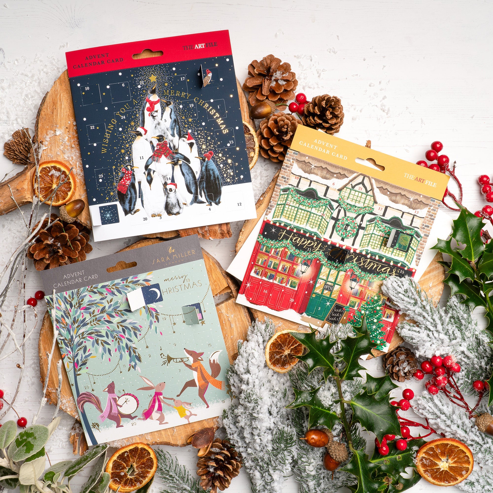 Three Christmas advent cards are displayed with festive decor on wooden wedges.