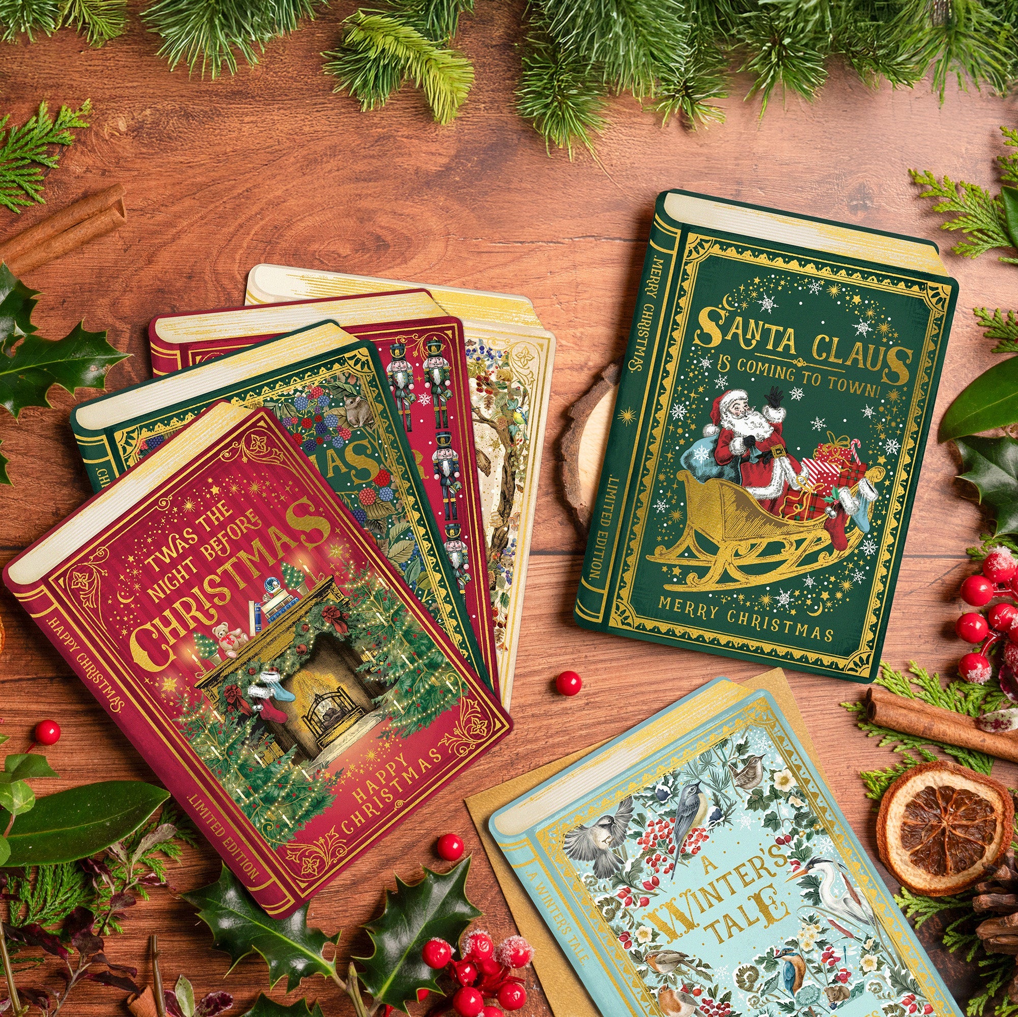 Christmas single cards shaped like festive books are laid out on a table with festive decorations.