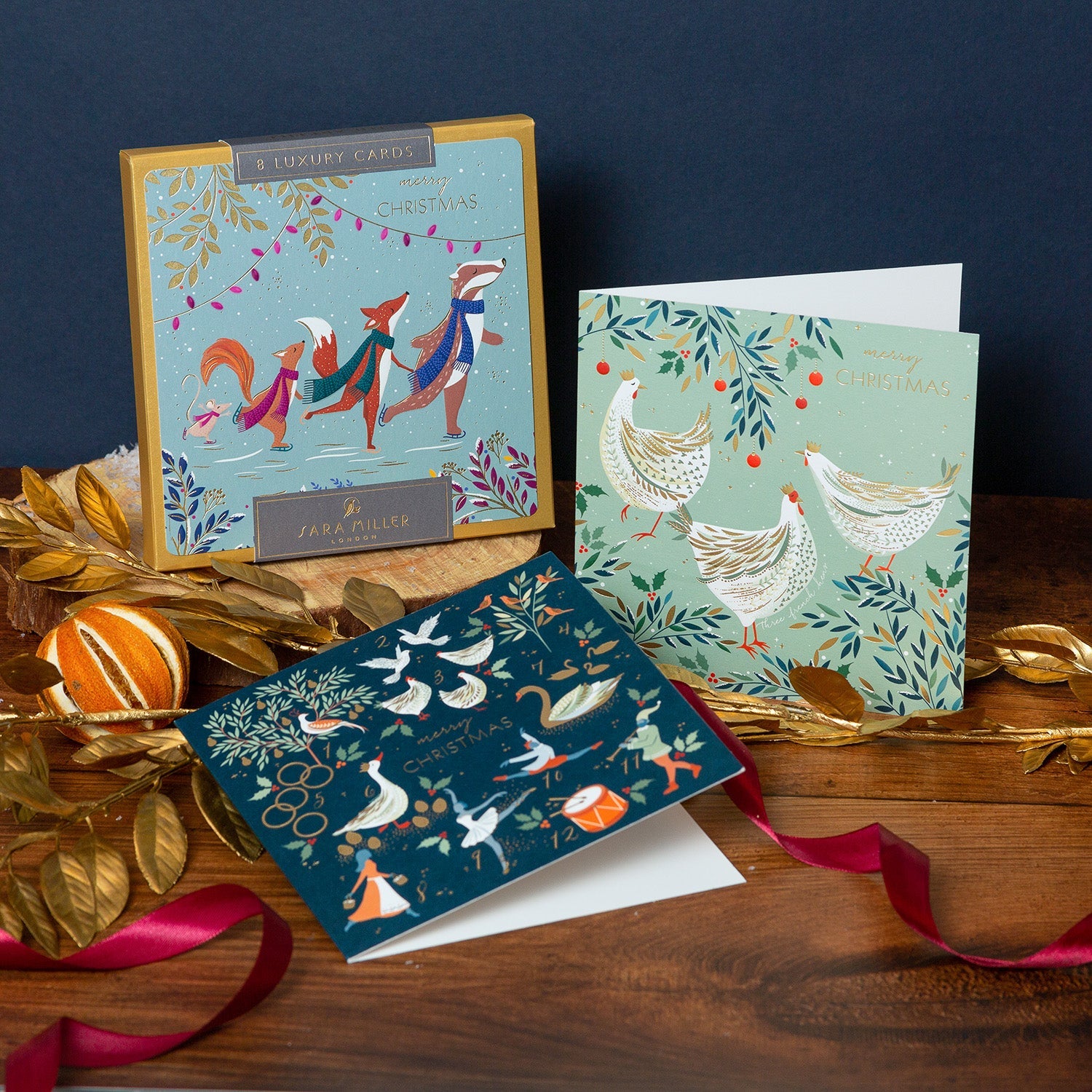 Luxury Christmas Card boxes on a wooden table surrounded by golden festive decorations.