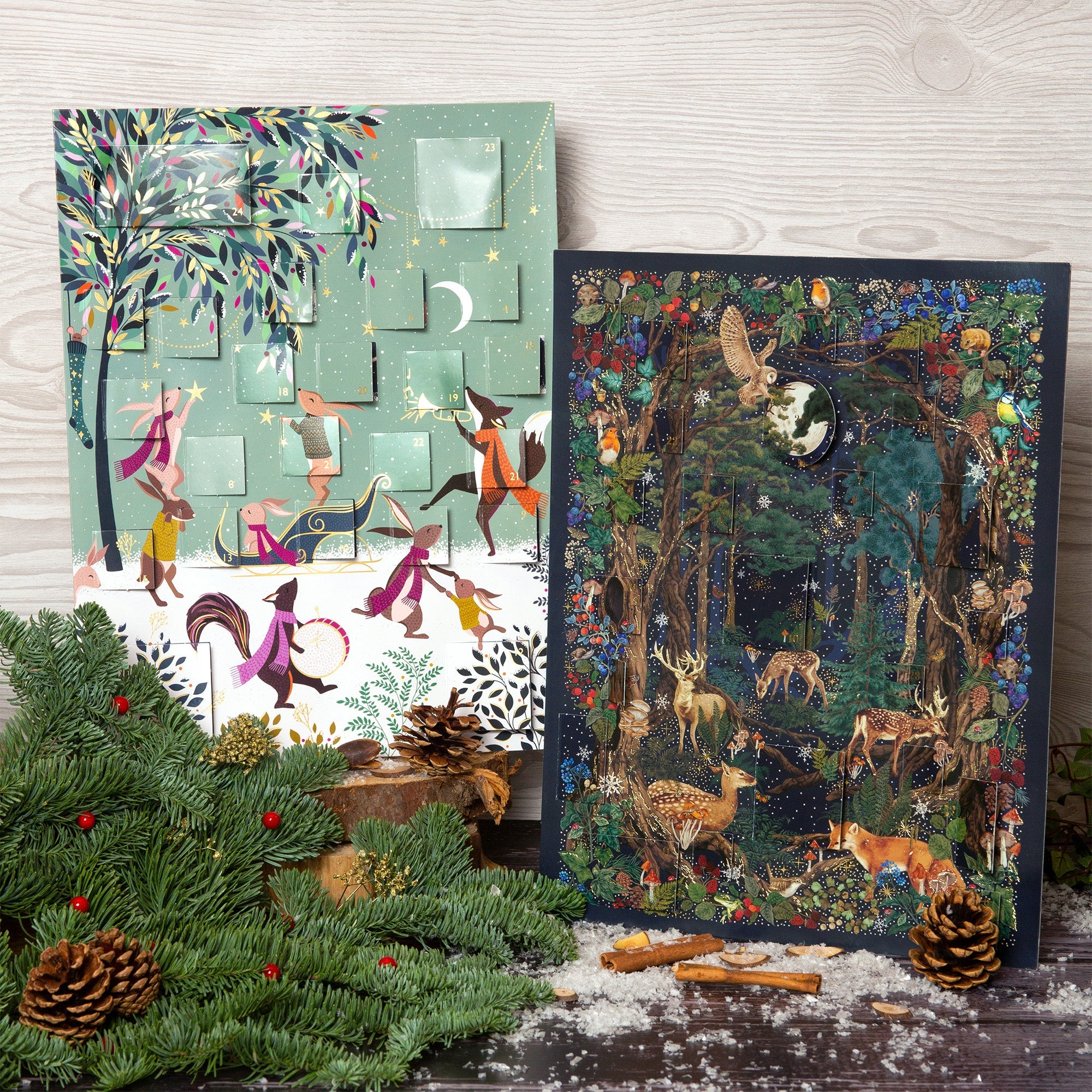 Two festive advent calendar featuring woodland scenes displayed with holly and pine cones.