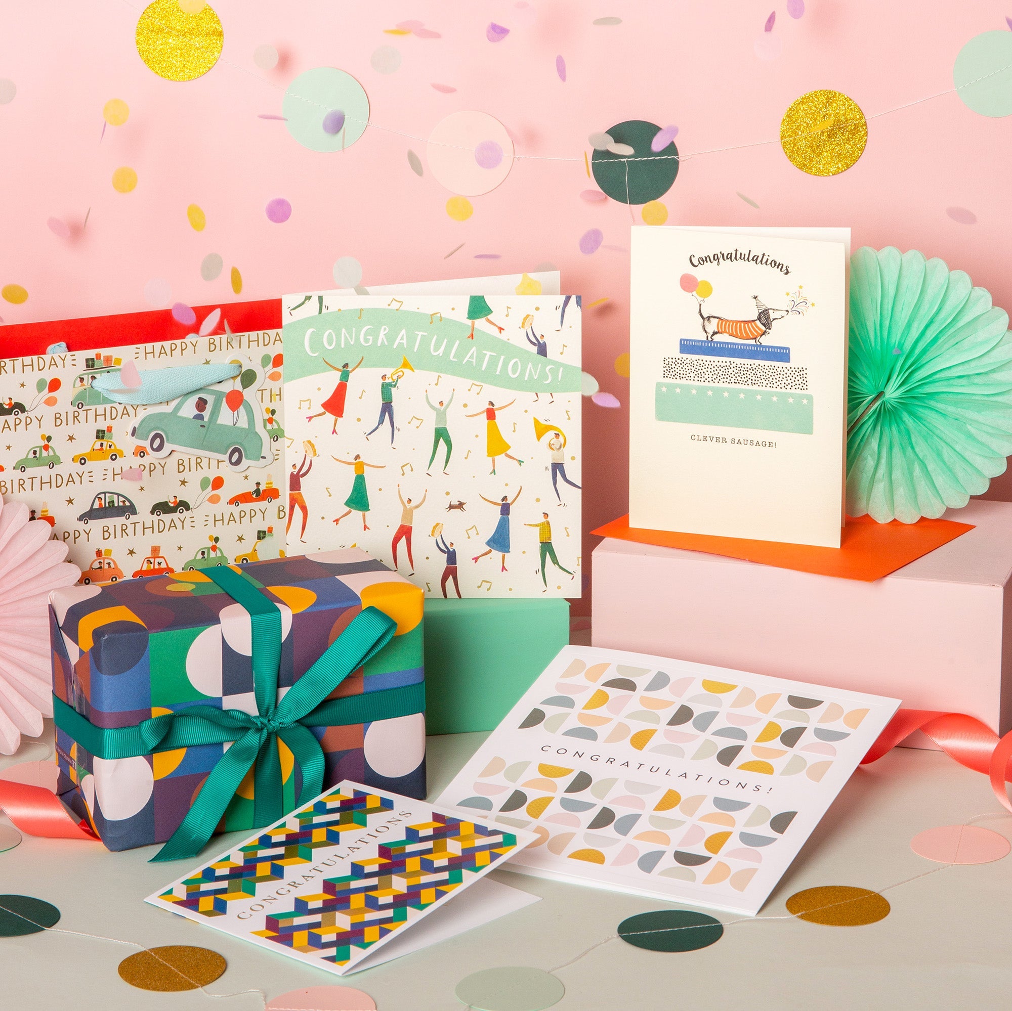 A collection of celebration cards, gift wrap and bags laid out on a table surrounded by confetti.