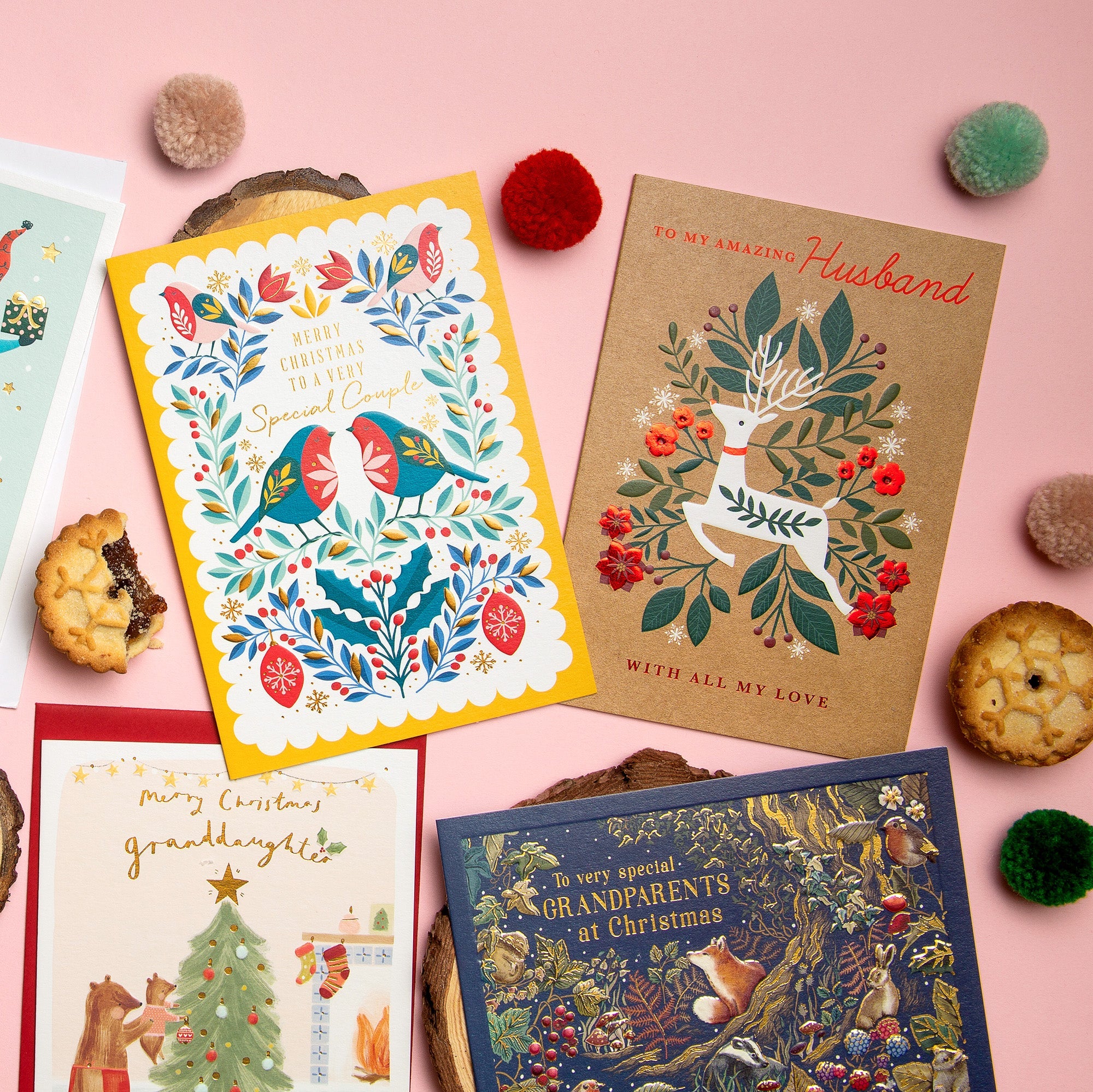 A selection of Christmas relation cards laid out on a pink backdrop, surrounded by mince pies.