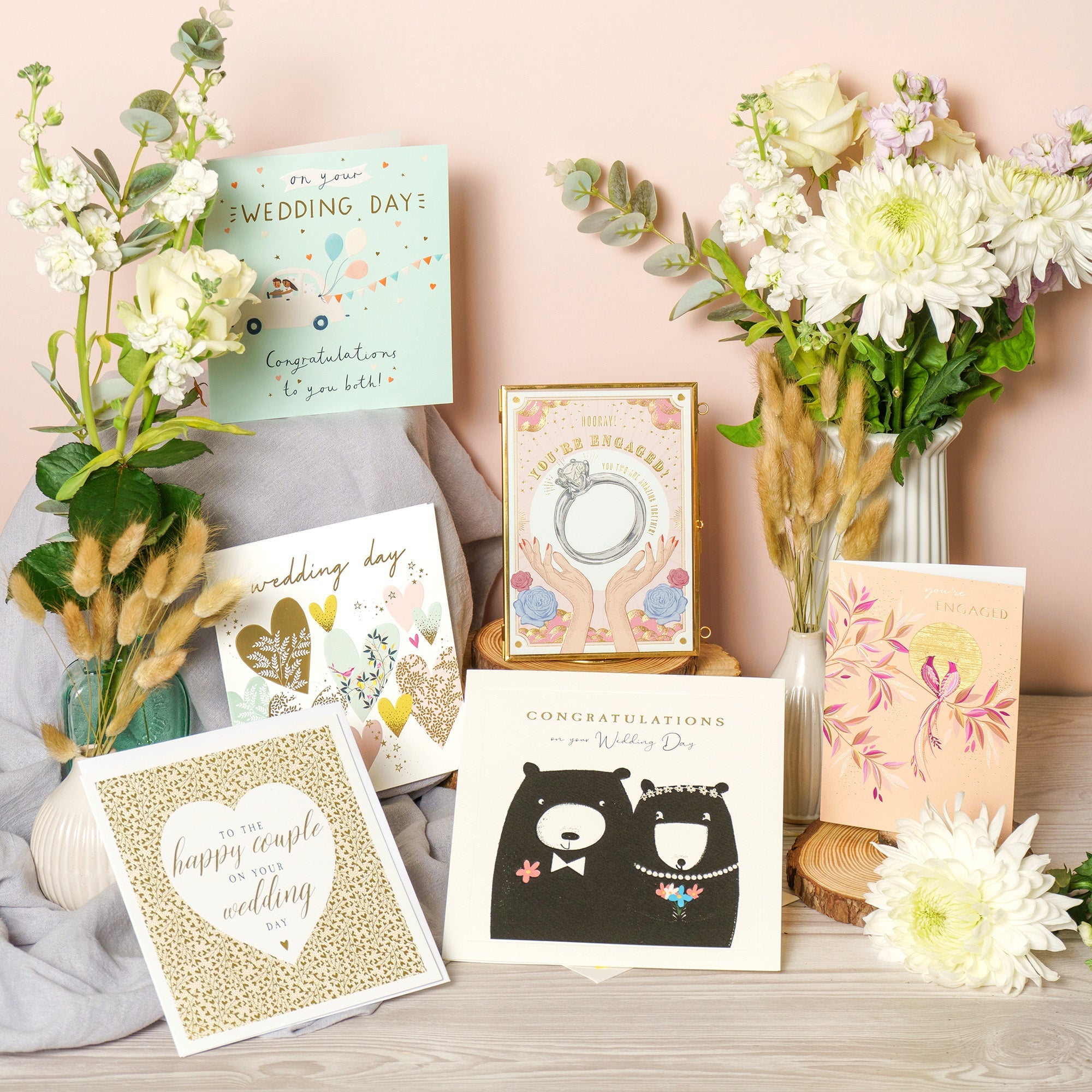 A selection of wedding and engagement cards are displayed on a table surrounded by flowers.