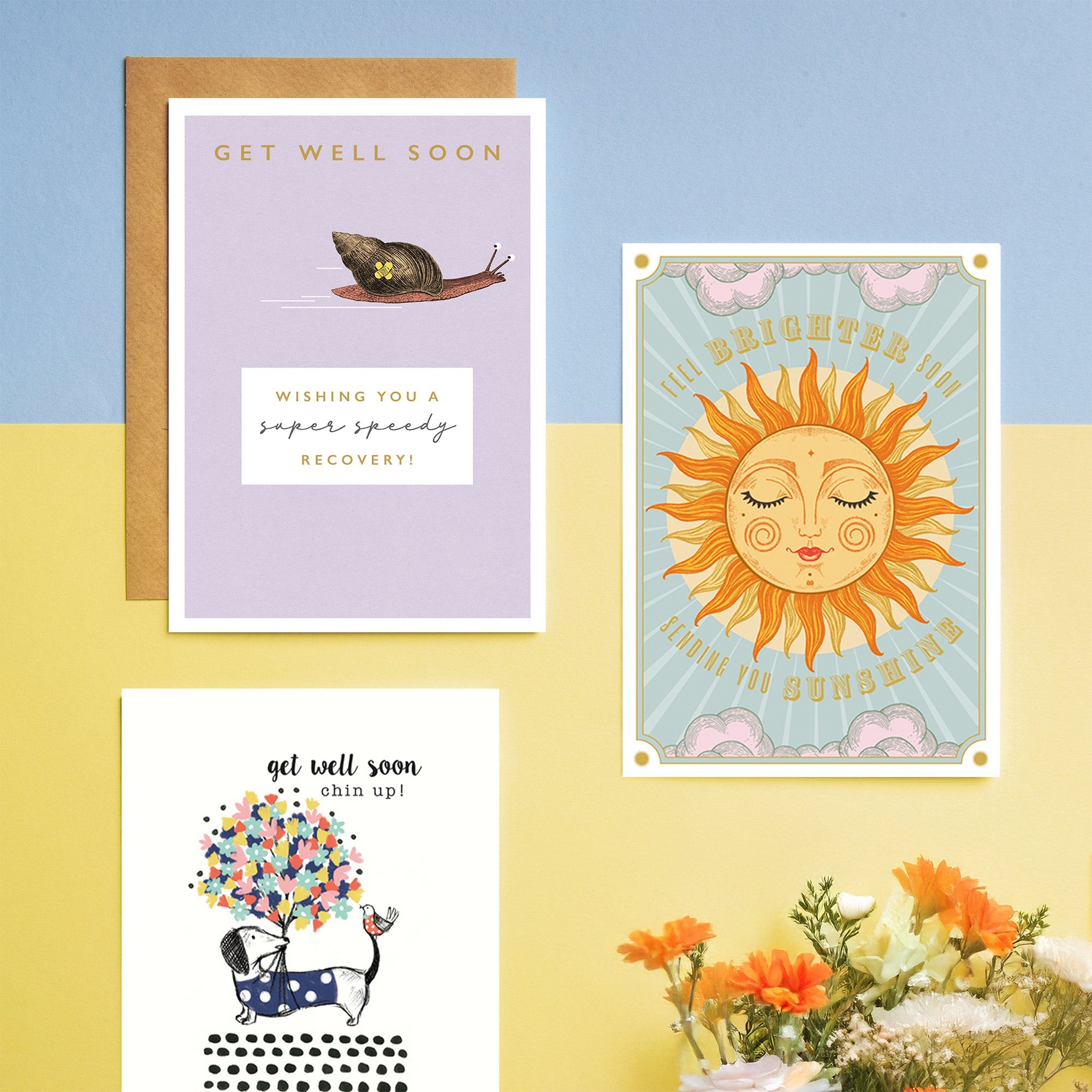 Three get well soon cards are laid on on colourful card, with flowers peeking into the picture from the bottom.