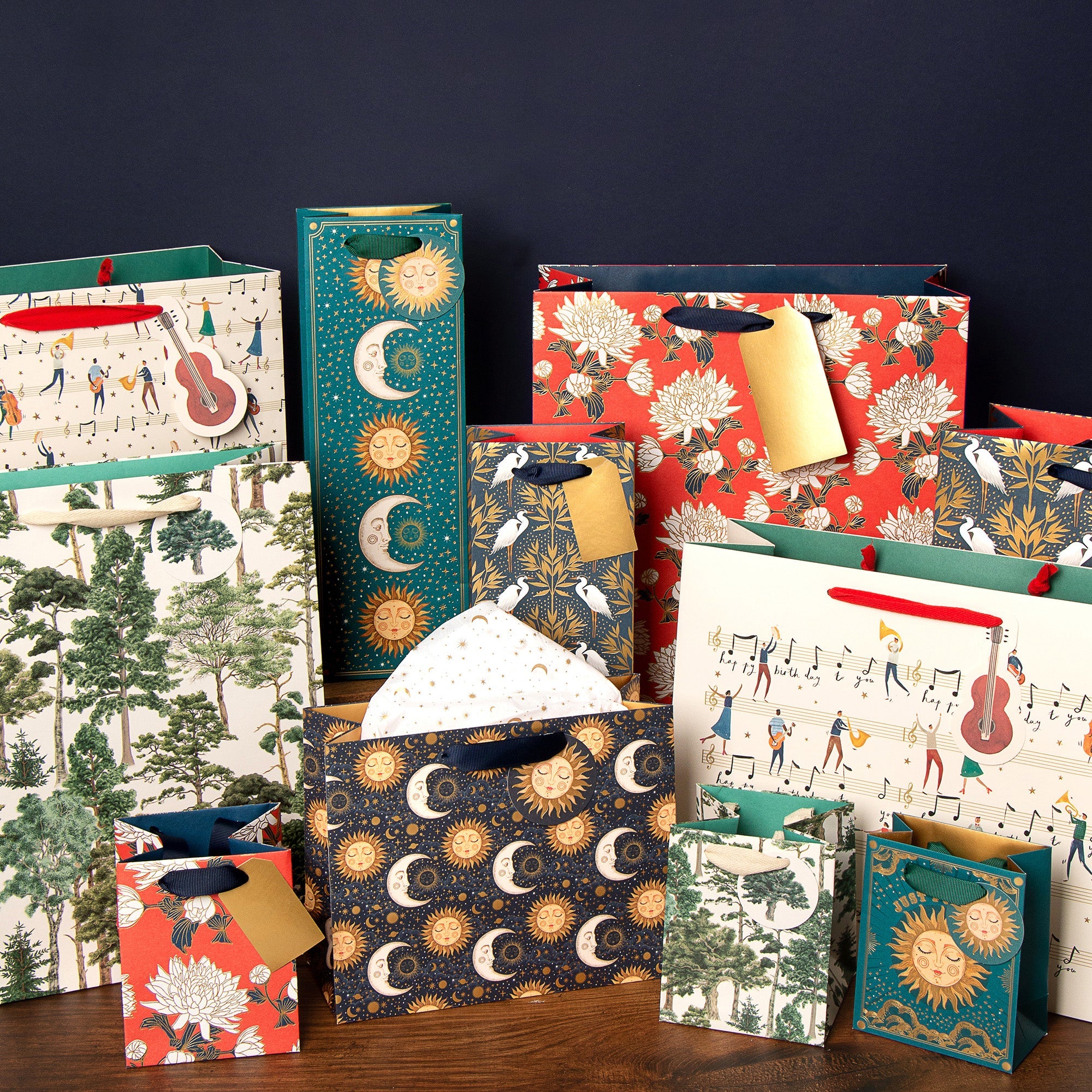 A collection of gift bags of all sizes and designs sit together on a table against a blue background.