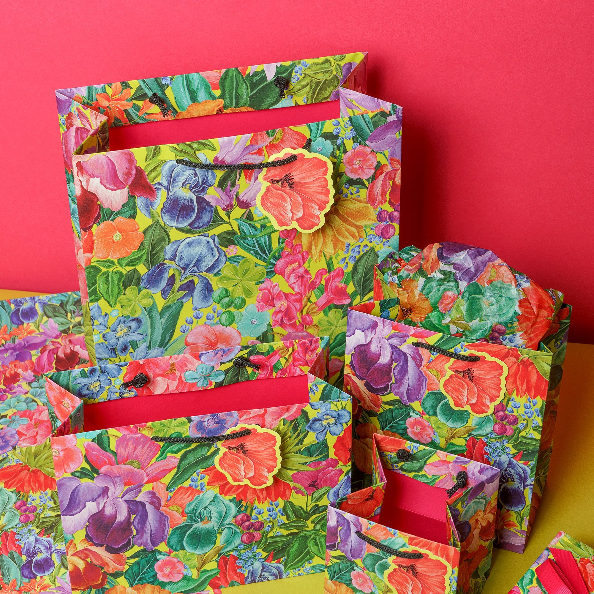 A selection of brightly patterned gift bag and wrap sit together against a pink background.