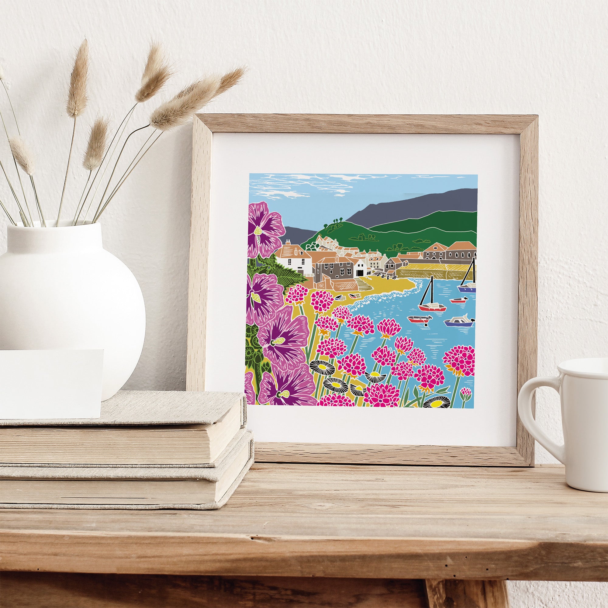 Framed artwork of a coastal scene with flowers on a wooden surface.