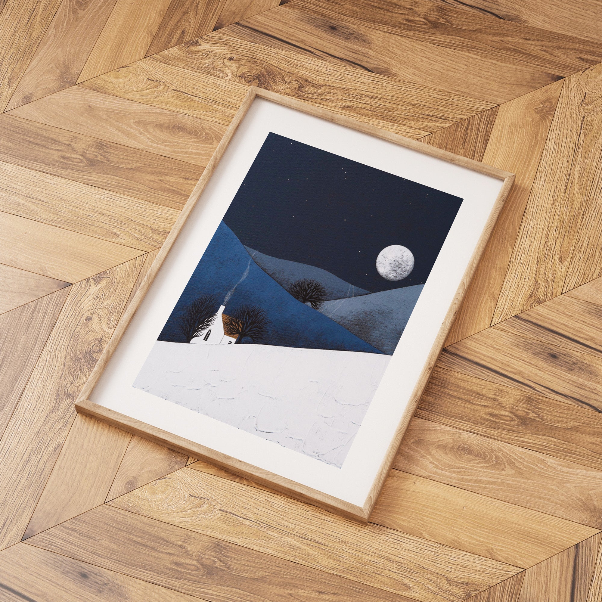 Framed artwork of a snowy landscape with a moonlit sky on a wooden floor.