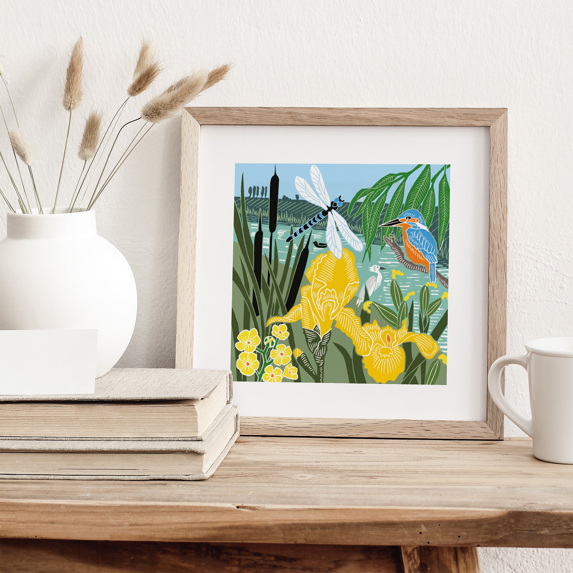 Framed artwork of a heron and dragonfly in a garden scene on a wooden surface.