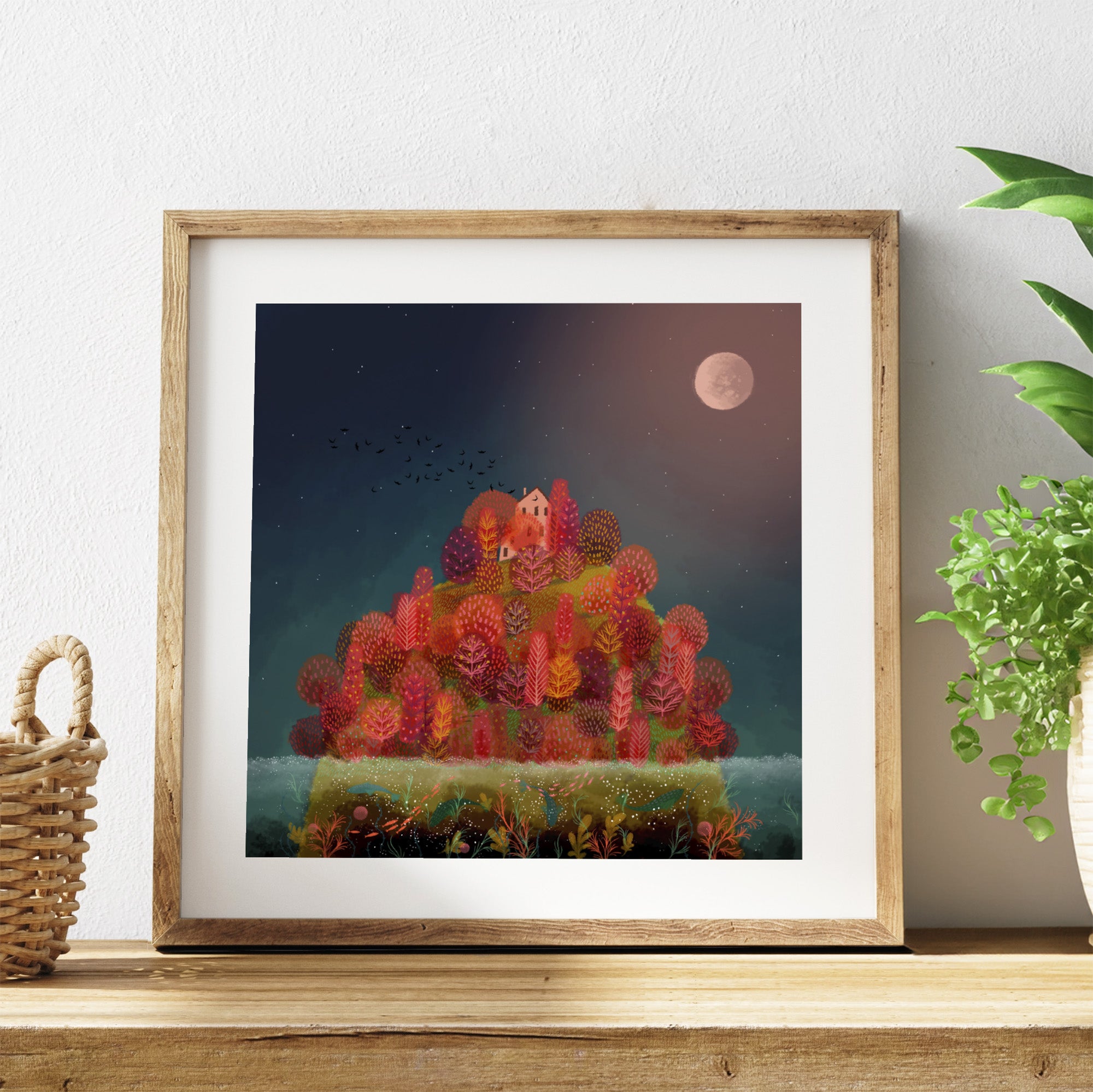 Framed artwork of an autumn night landscape with houses and trees on a shelf.