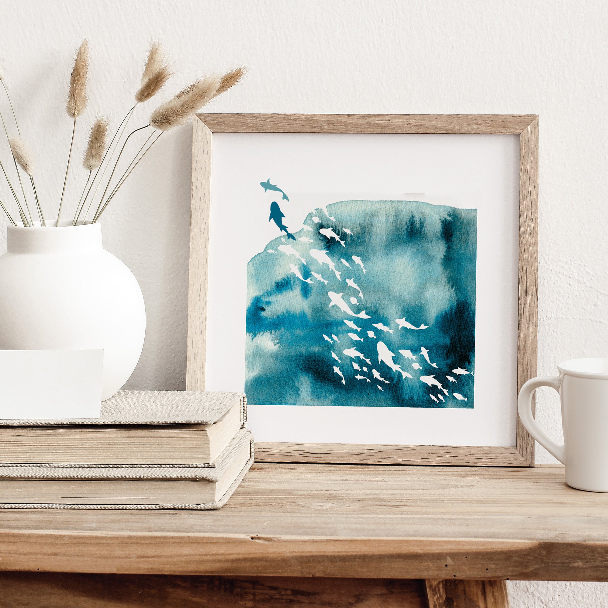 Framed artwork of a blue and white abstract design on a wooden surface with a vase and books.