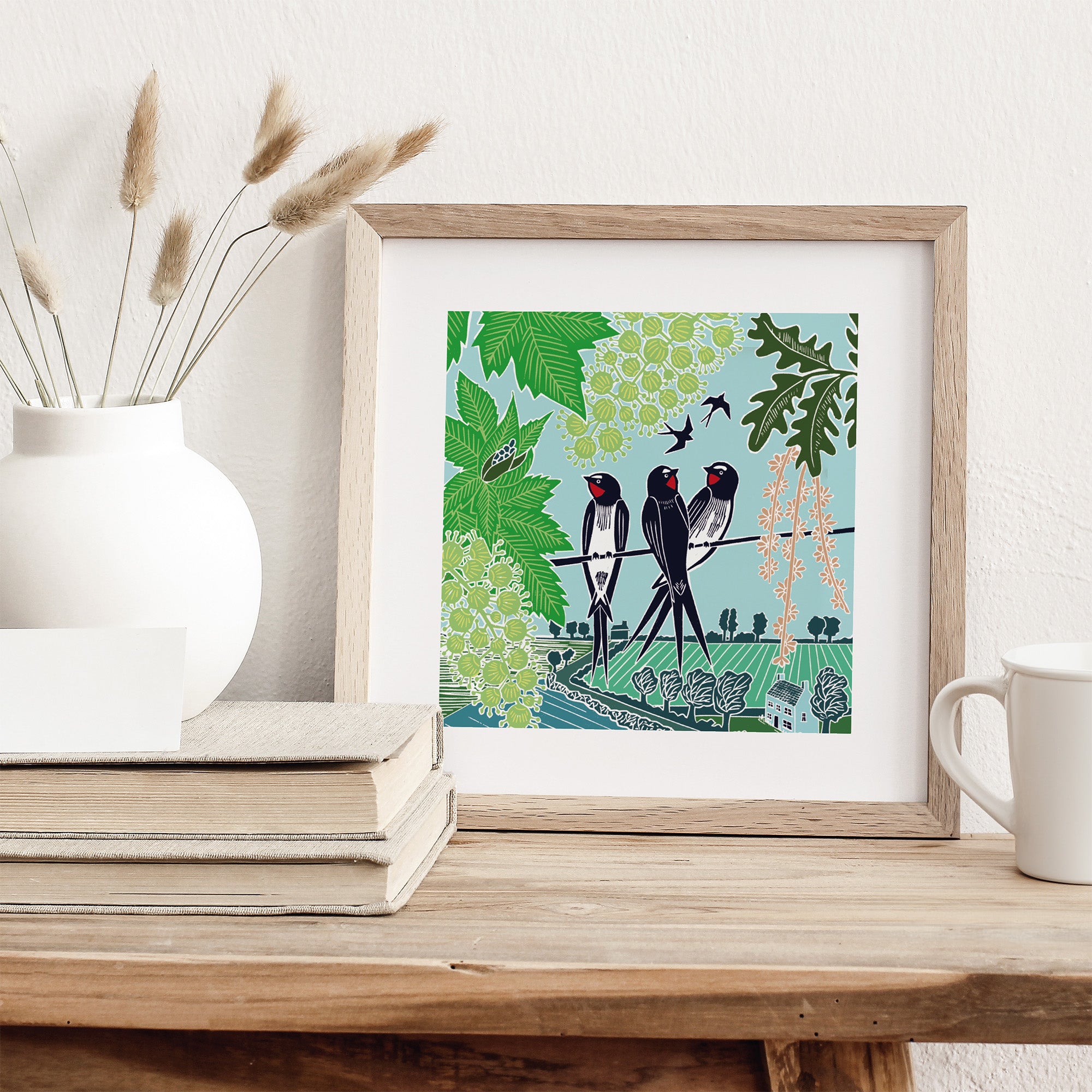 Framed artwork of birds on a branch with leaves and flowers, displayed on a wooden surface.