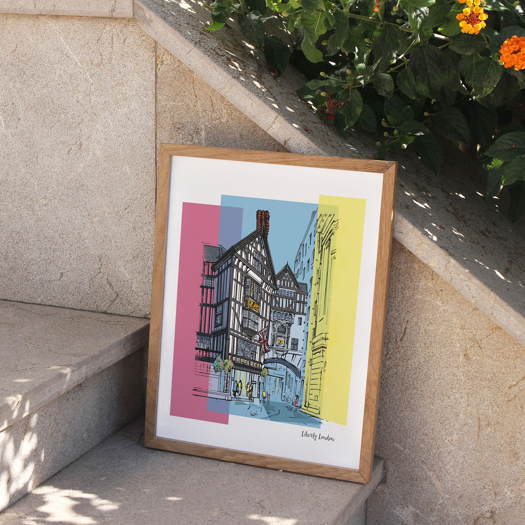 Framed artwork of a colorful building on a stone ledge with plants in the background.