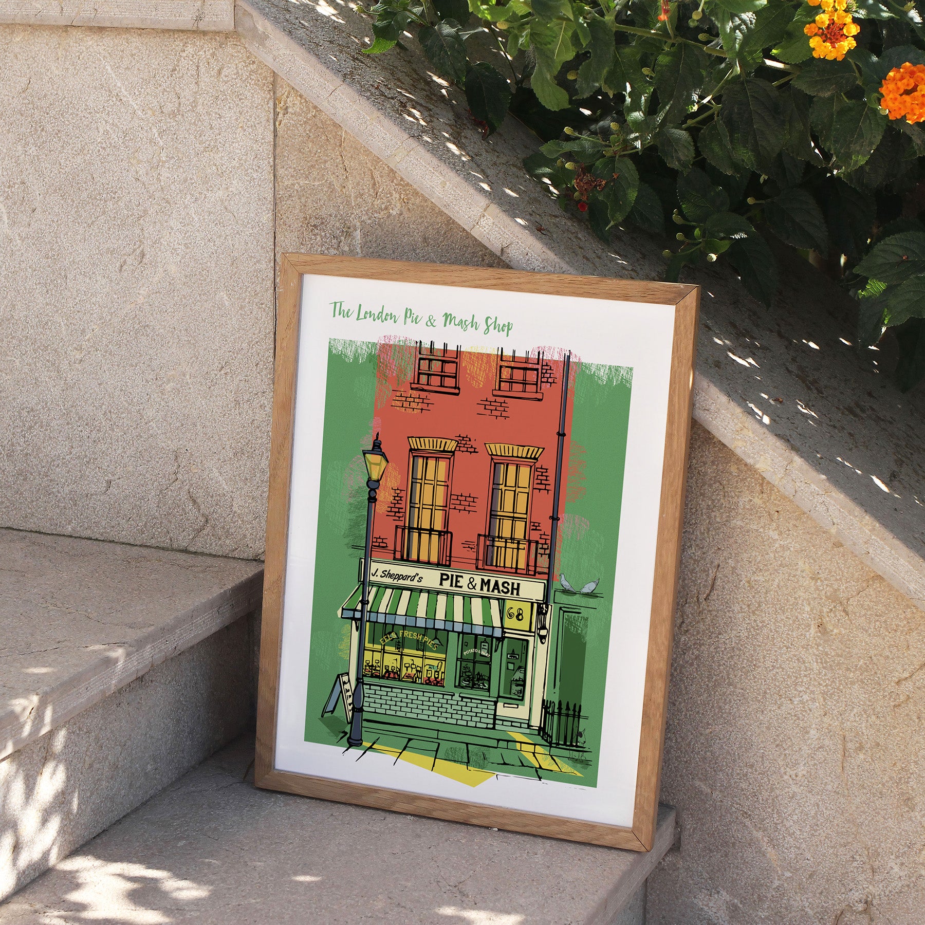 Framed artwork of a pie and mash shop on a stone ledge with plants in the background.