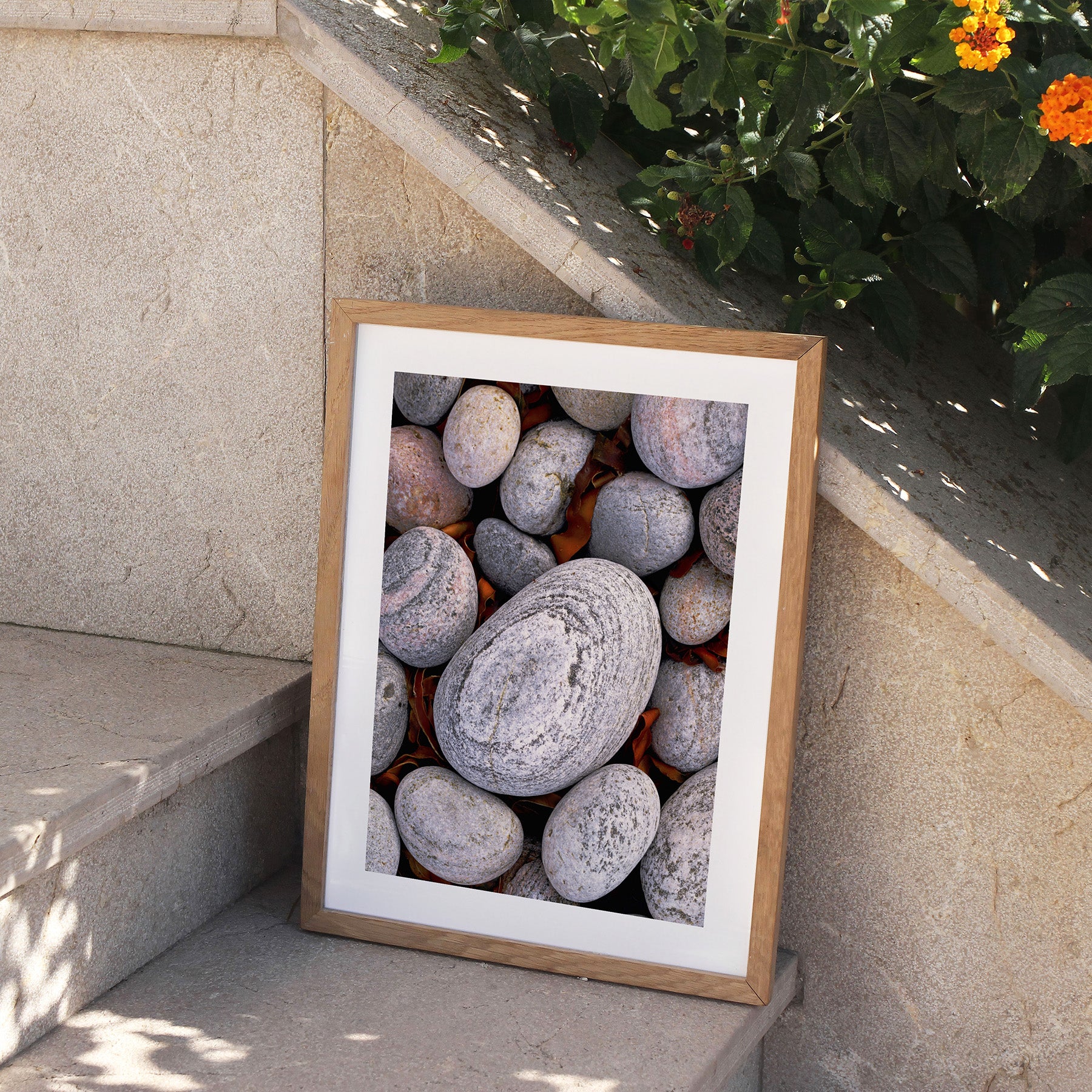 Framed simplistic photography art print featuring a close of up of pebbles found on a beach, perched on stone steps, outside.