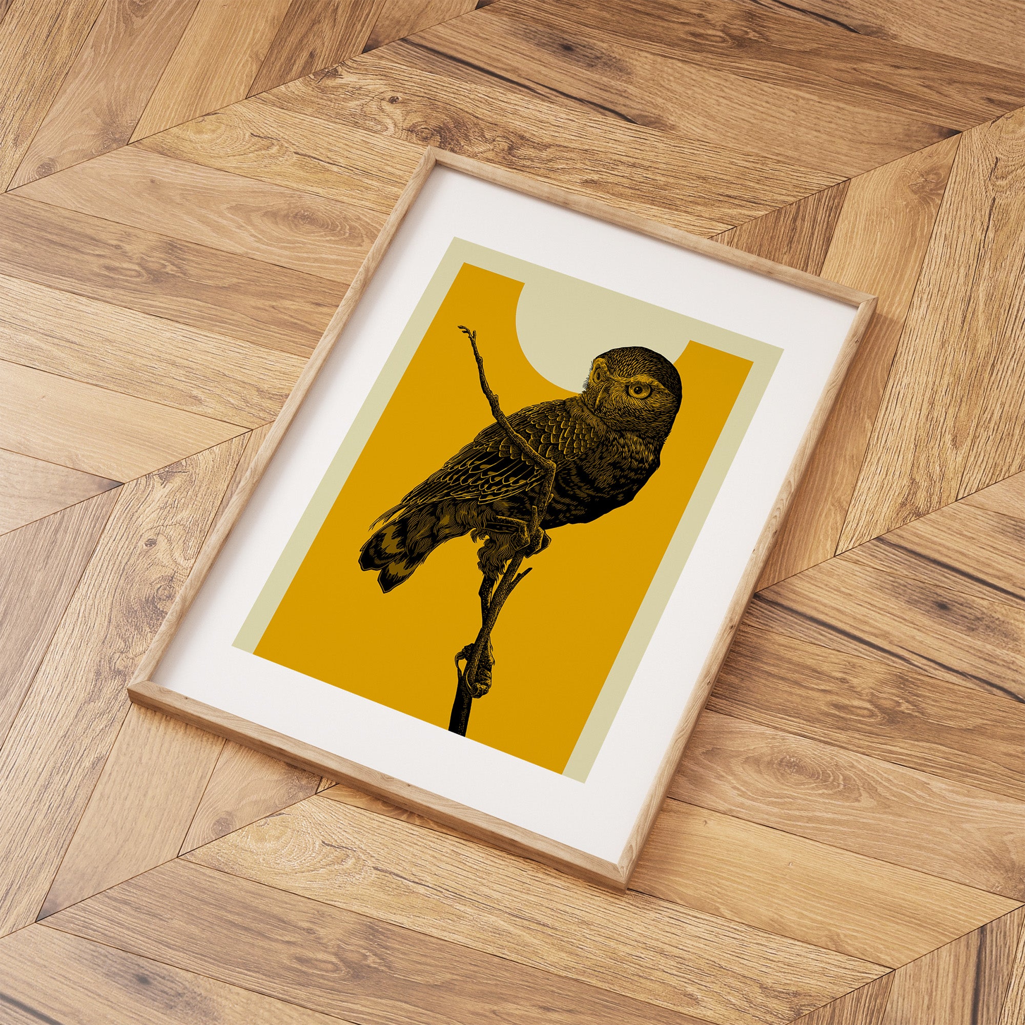 Framed print featuring a detailed illustration of an owl perched on a branch, in front of a vibrant yellow sky. Print is laid out on a wooden floor.