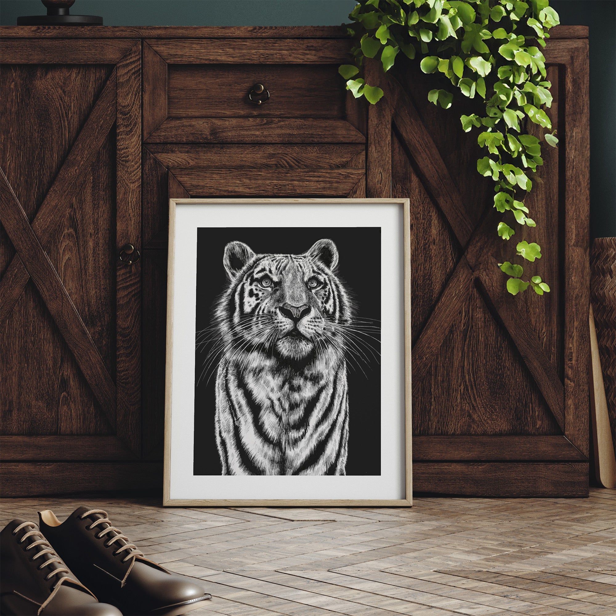 Framed art print featuring a detailed illustration of a tiger gazing upwards, in black and white. Print is leaning against a dresser.