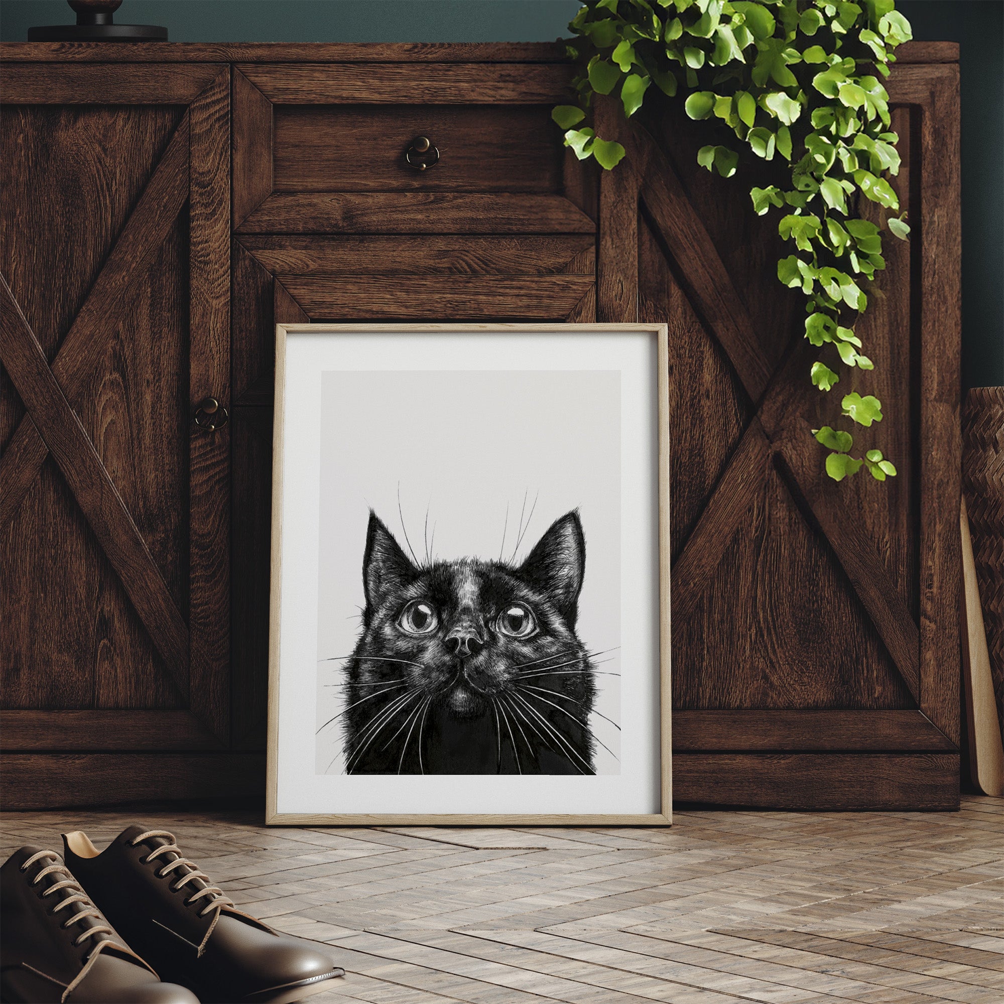 Framed monochrome art print featuring a detailed illustration of a black cat. Print is leaning on a dresser.