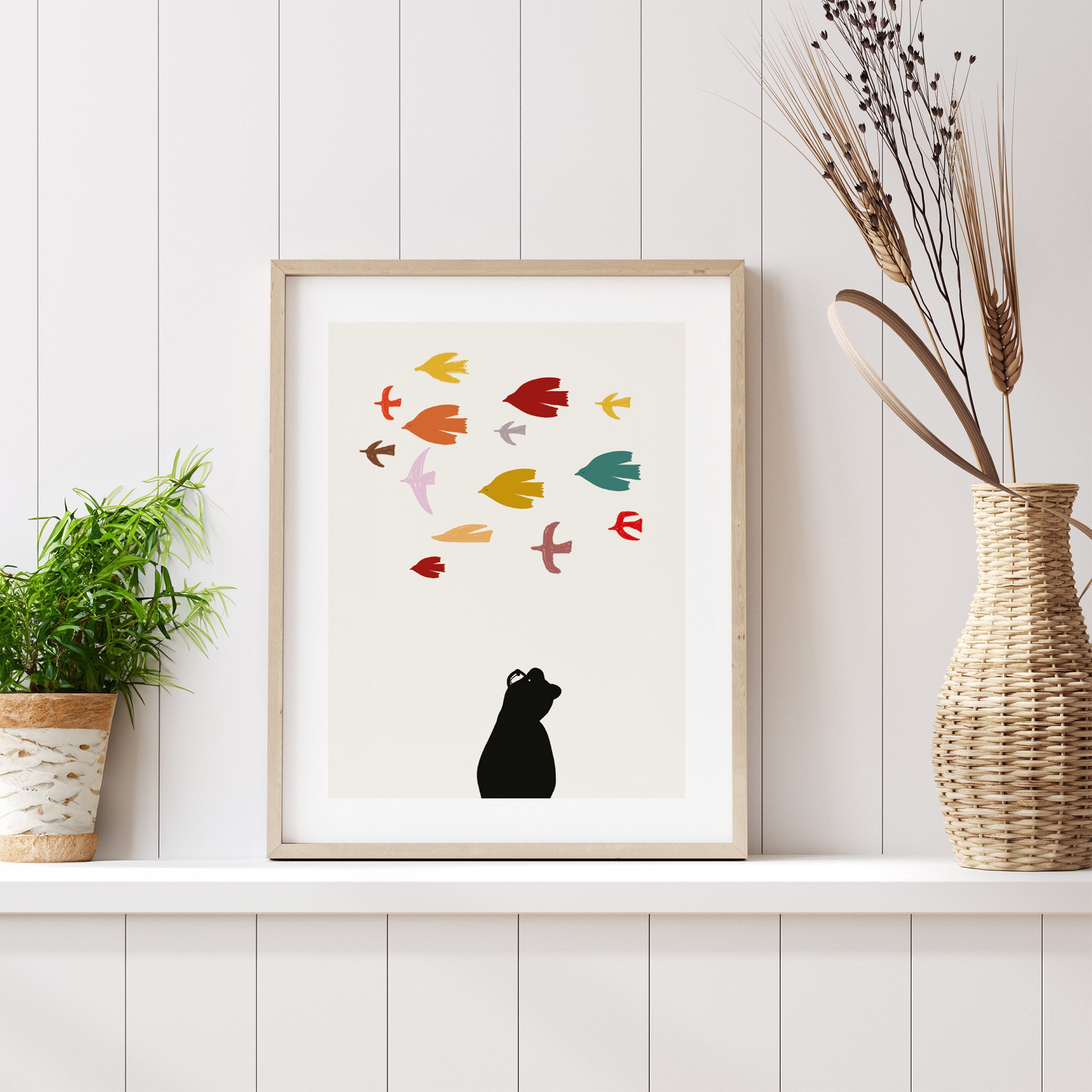 Framed artwork with colorful abstract designs and a black silhouette on a white wall.