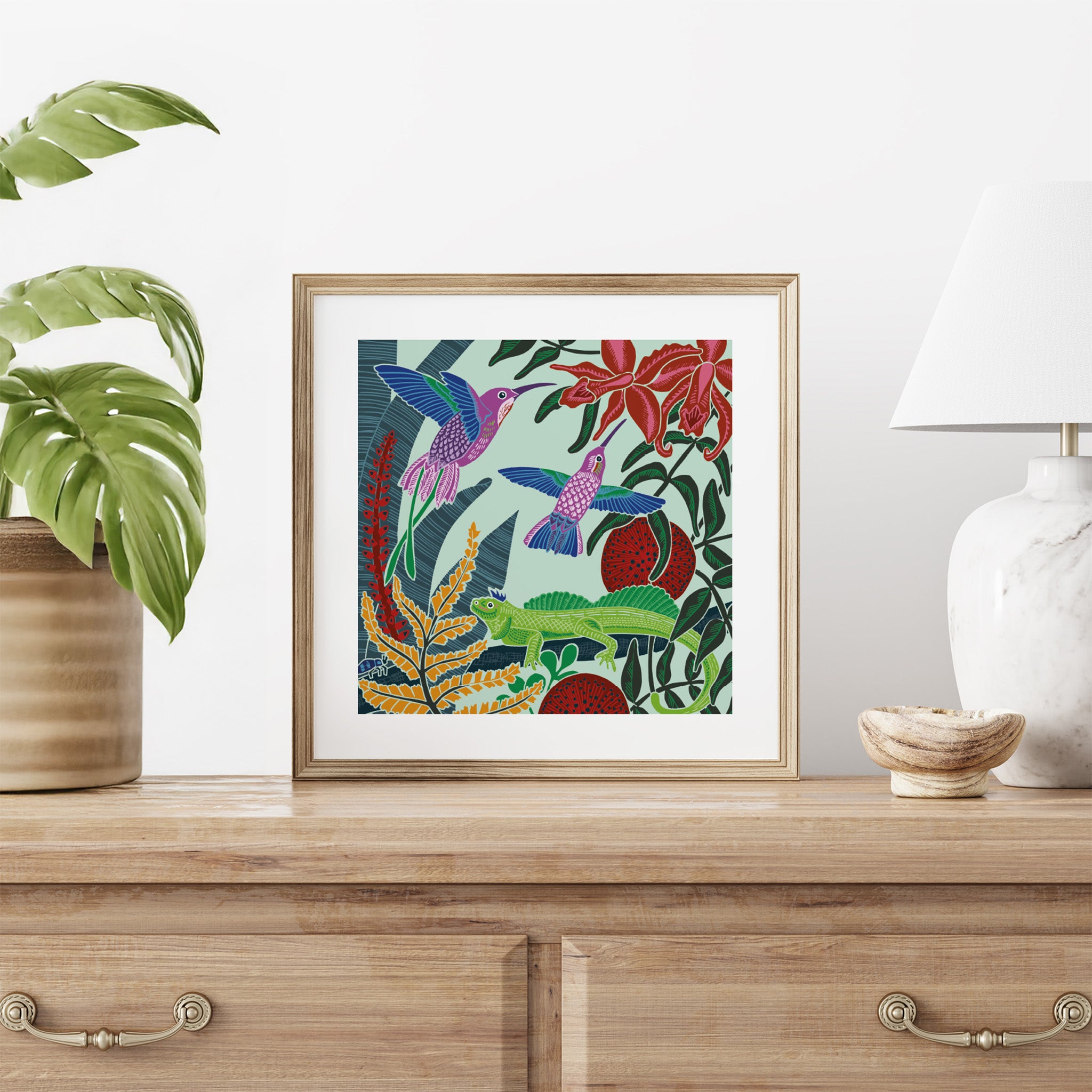 Framed artwork with colorful birds and plants on a wooden surface with decor items.