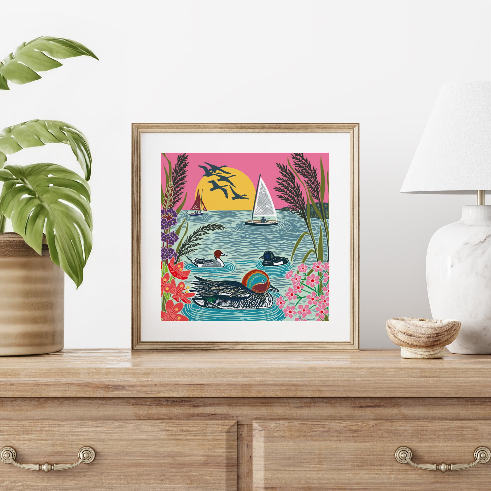 Framed artwork of ducks and a sailboat on a wall above a wooden cabinet.