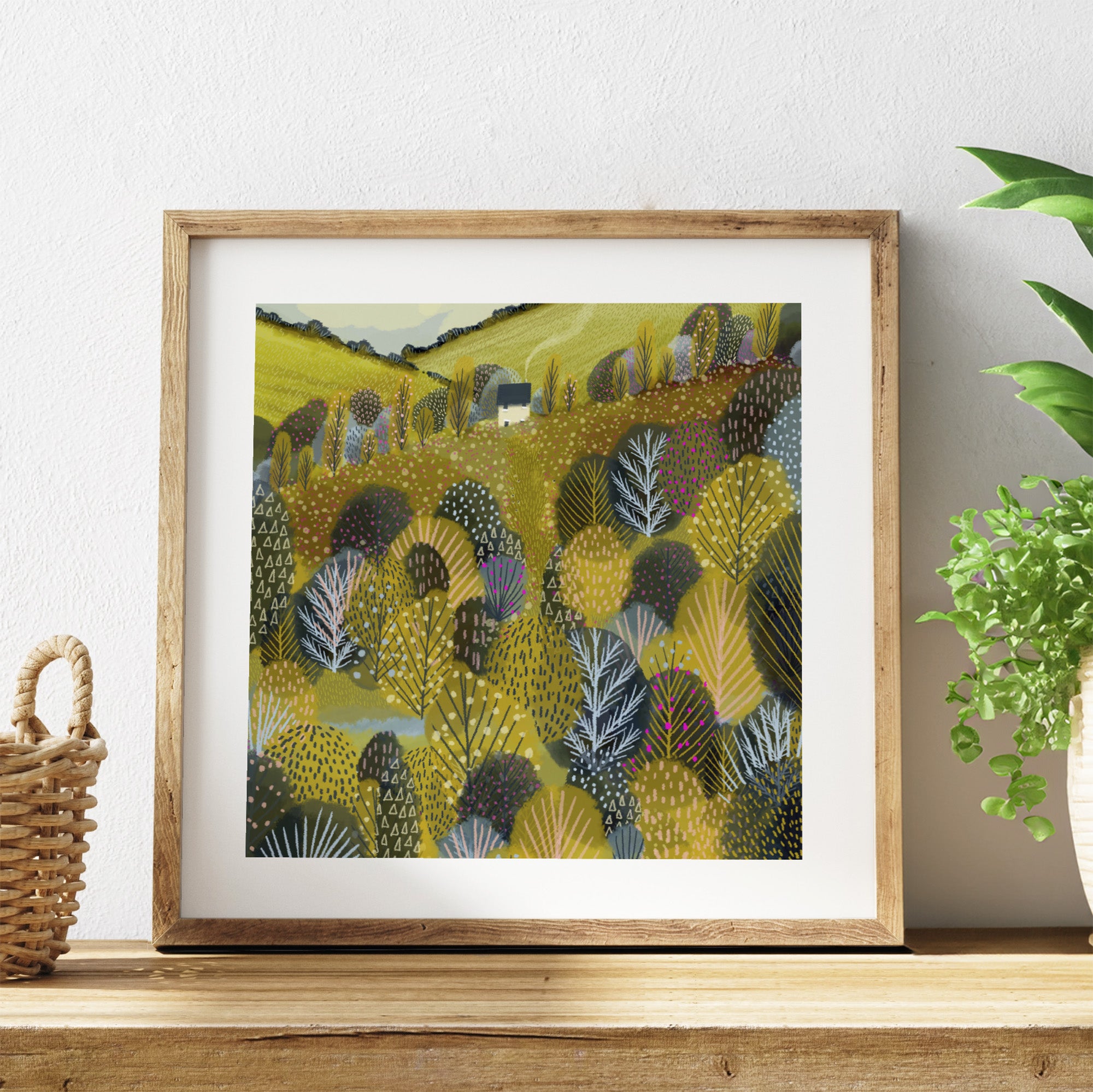 Framed artwork with a colourful landscape design on a wooden shelf.