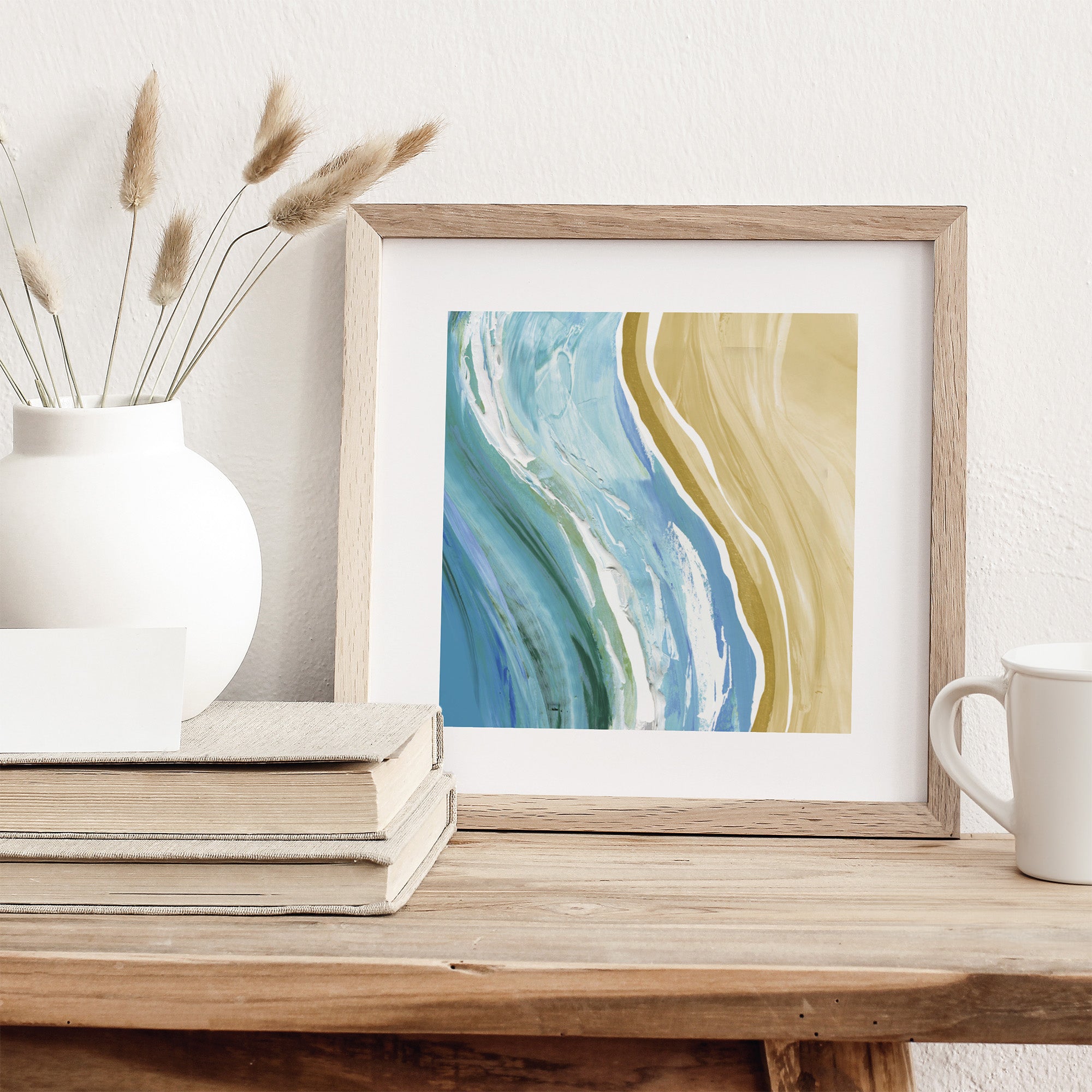 Art print featuring a watercolour scene of waves next to a beach. Art print is stood on a dresser.