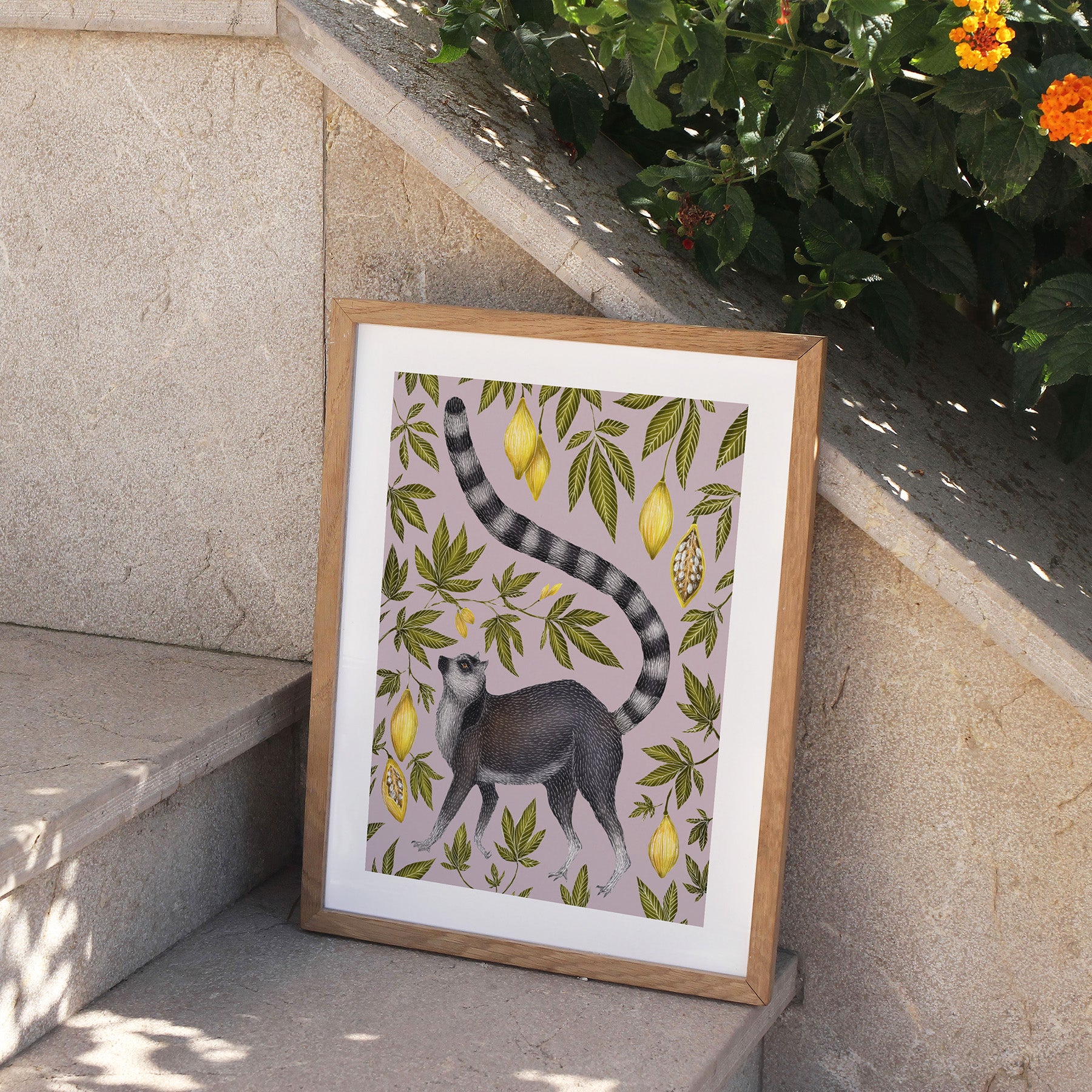 Framed artwork of a lemur and lemon pattern on a stone ledge with plants.