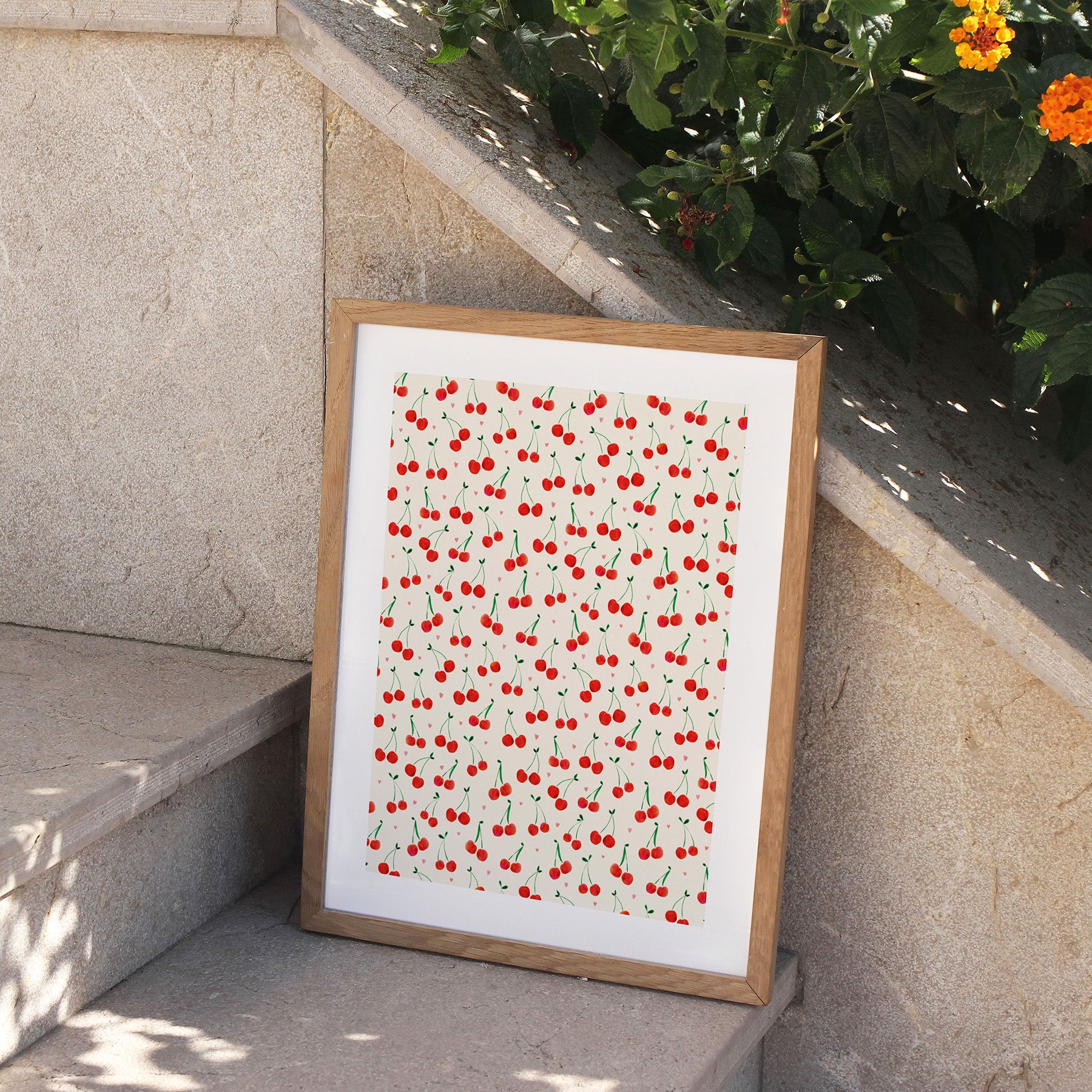 Framed art print of a pattern of red cherries on a white background. Print is displayed on outside steps.