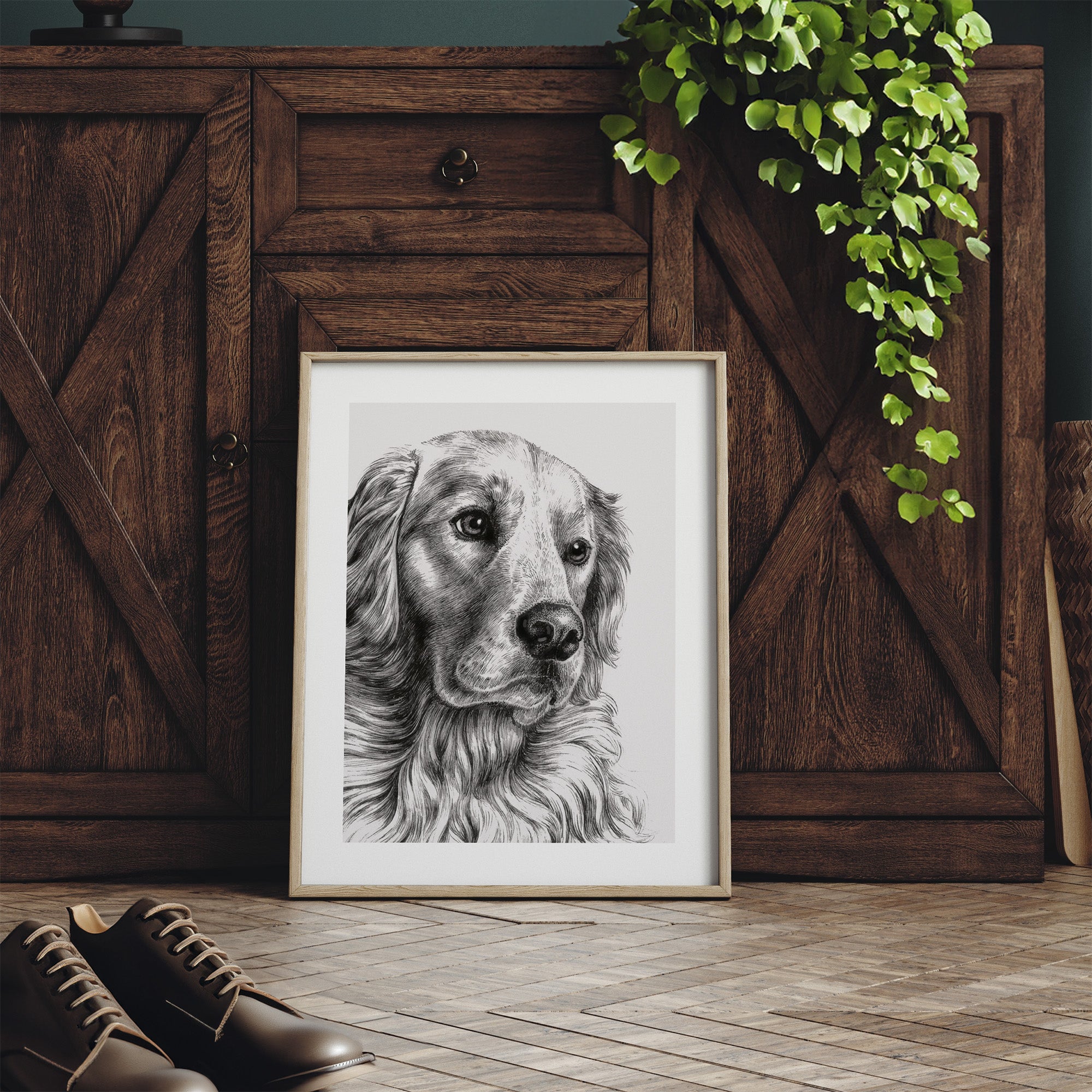 Framed black and white dog portrait on a wooden floor with a wooden cabinet and plant in the background.