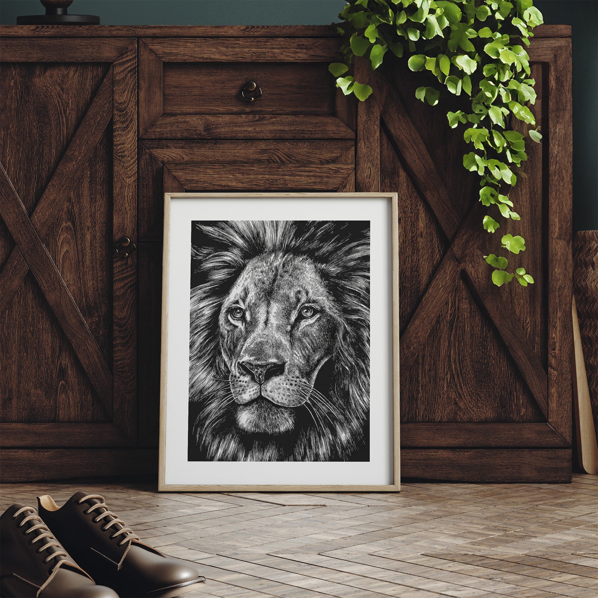Framed black and white lion portrait on a wooden floor with a wooden cabinet and plant in the background.