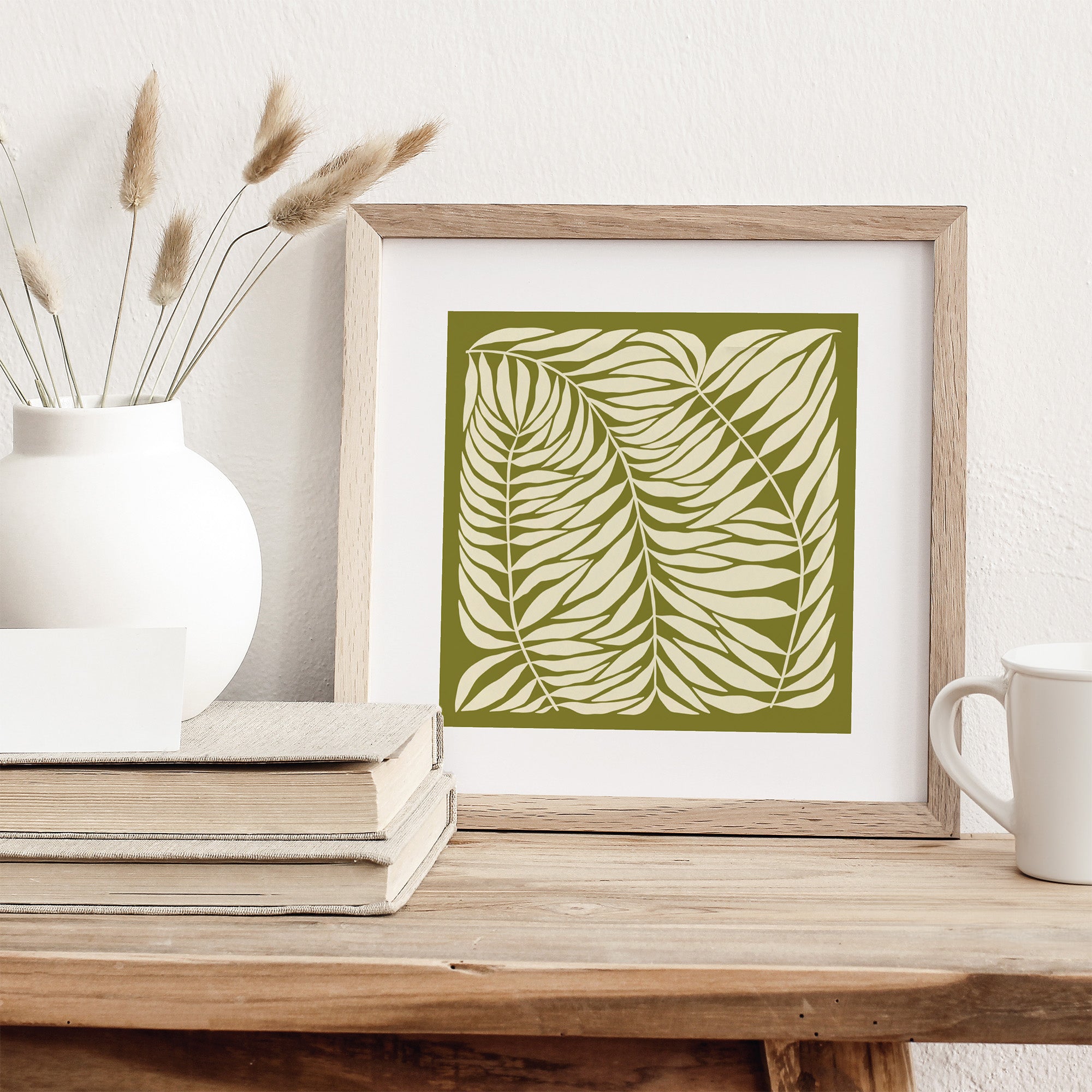 Framed artwork with leaf design on a wooden surface with decor items.