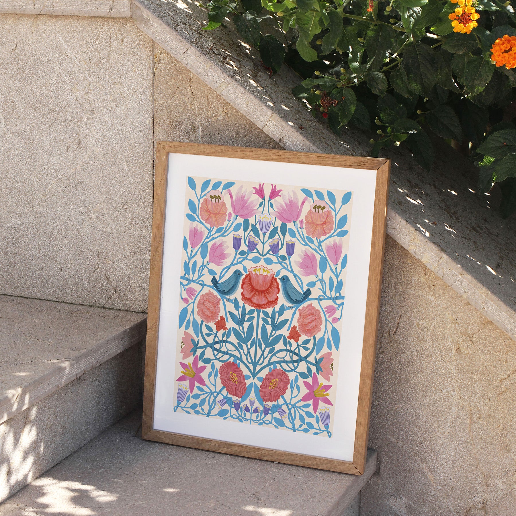 Framed floral artwork on a stone ledge with plants in the background.