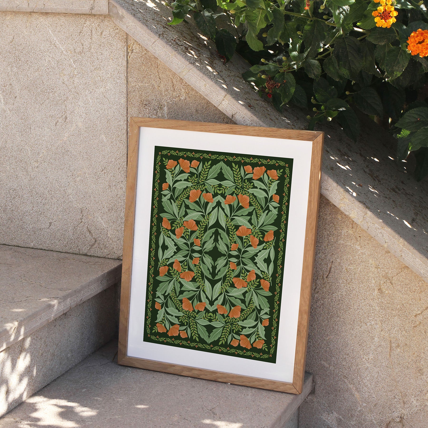 Framed artwork with a green and orange pattern on a stone ledge with plants in the background.