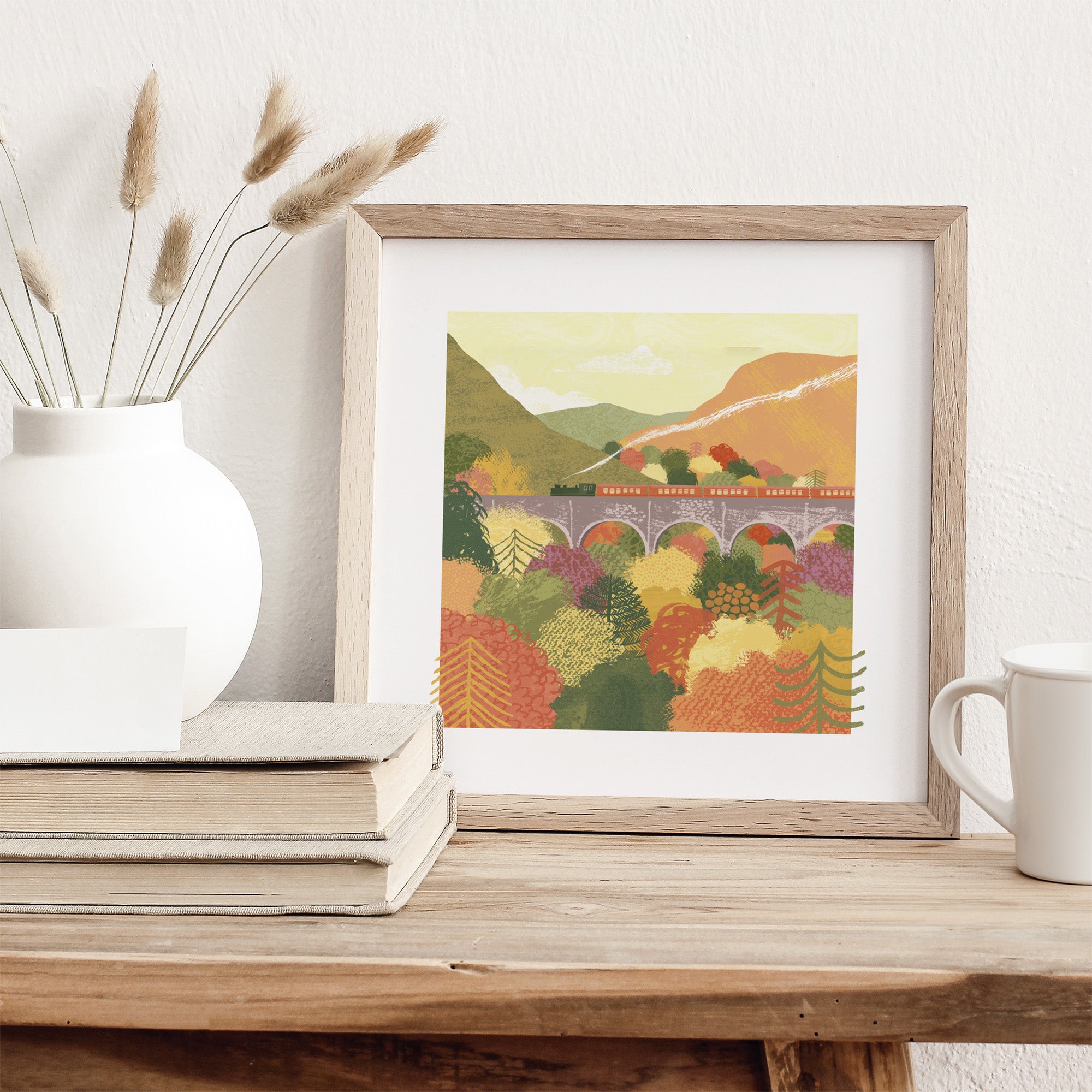 Framed artwork of a scenic landscape with a bridge on a wooden surface.