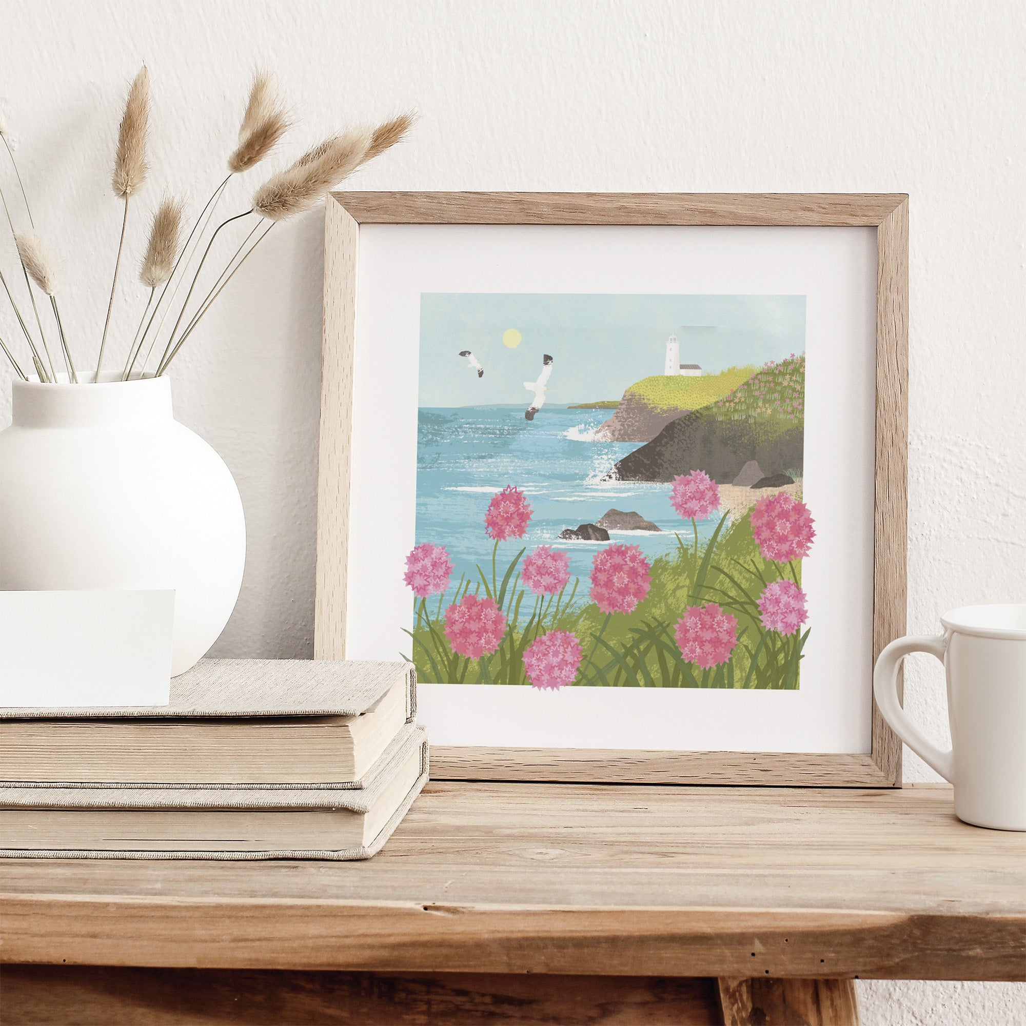 Framed artwork of a coastal scene with pink flowers on a wooden surface.