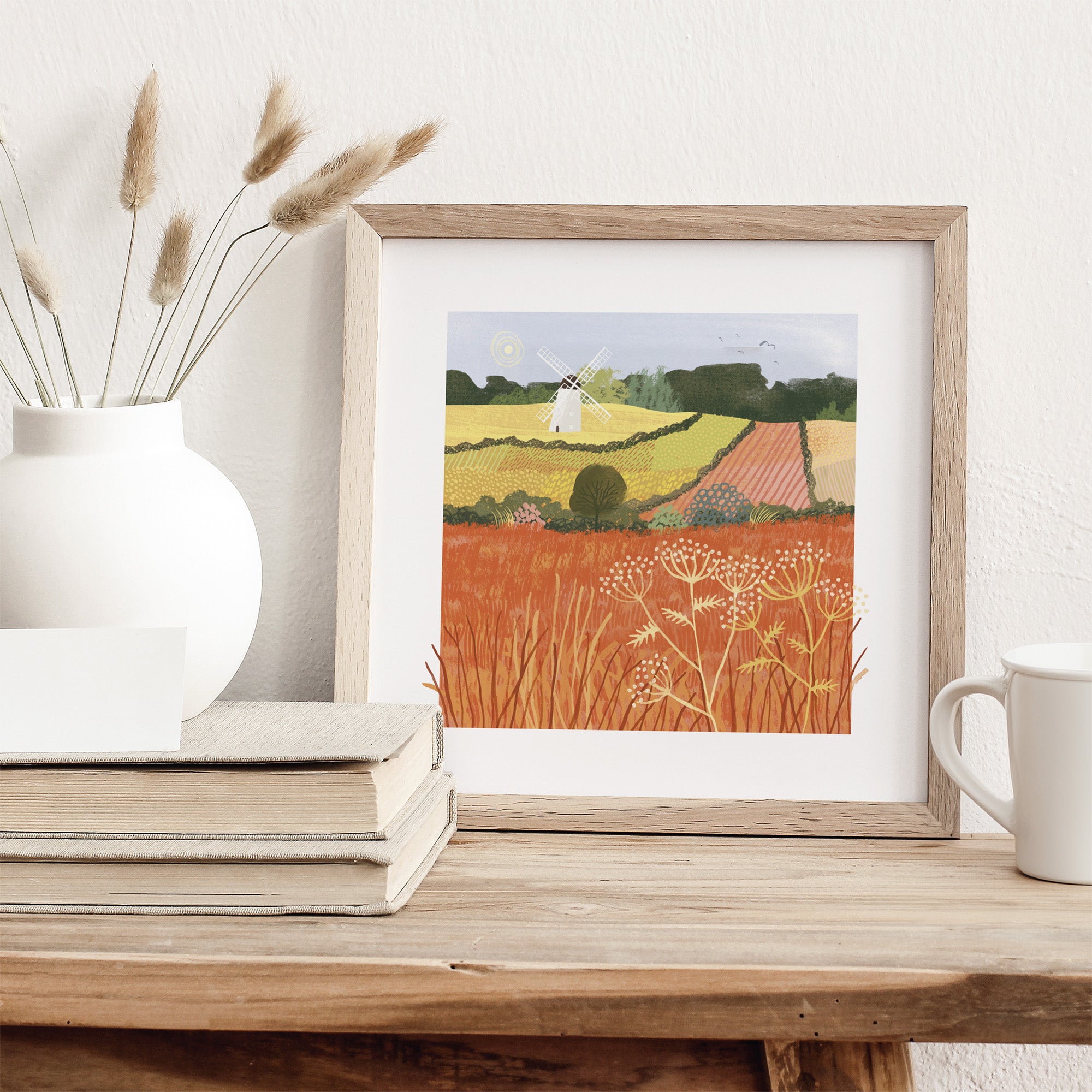 Framed artwork of a landscape with a person in a field on a wooden table.