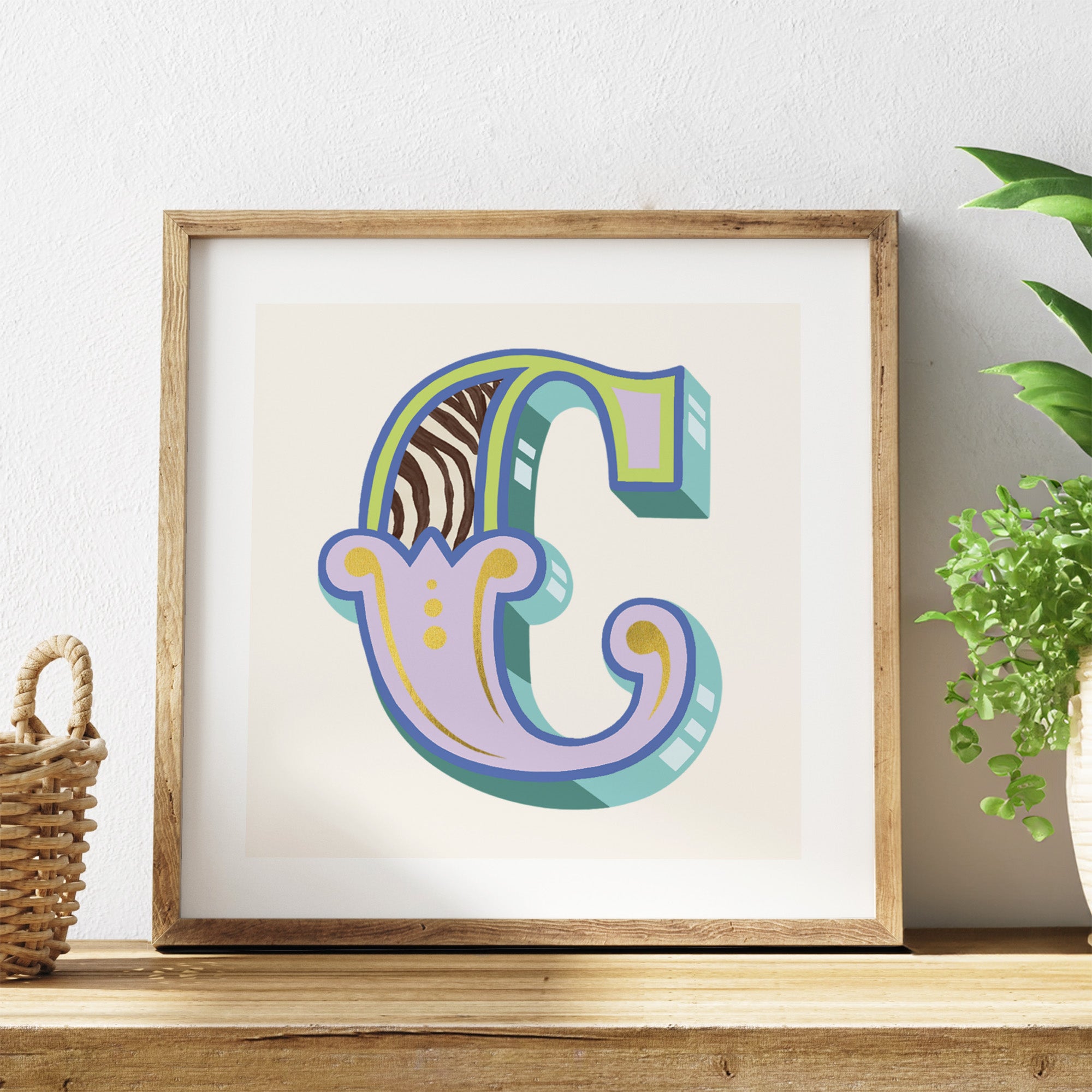 Framed artwork with a colourful letter 'C' on a white background, placed on a wooden surface with a plant in the corner.
