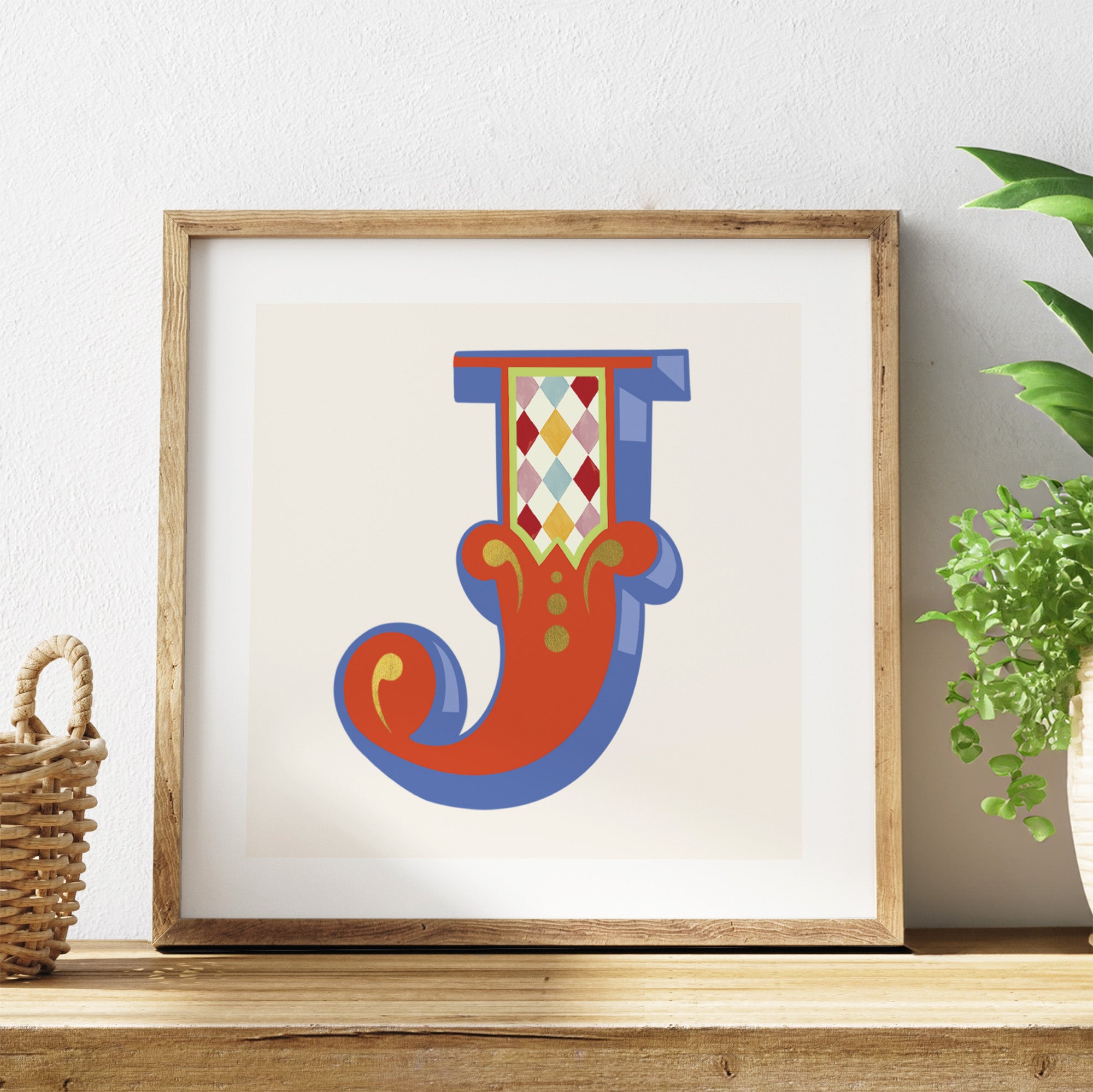 Framed colourful letter 'J' artwork on a shelf with a plant in the background.