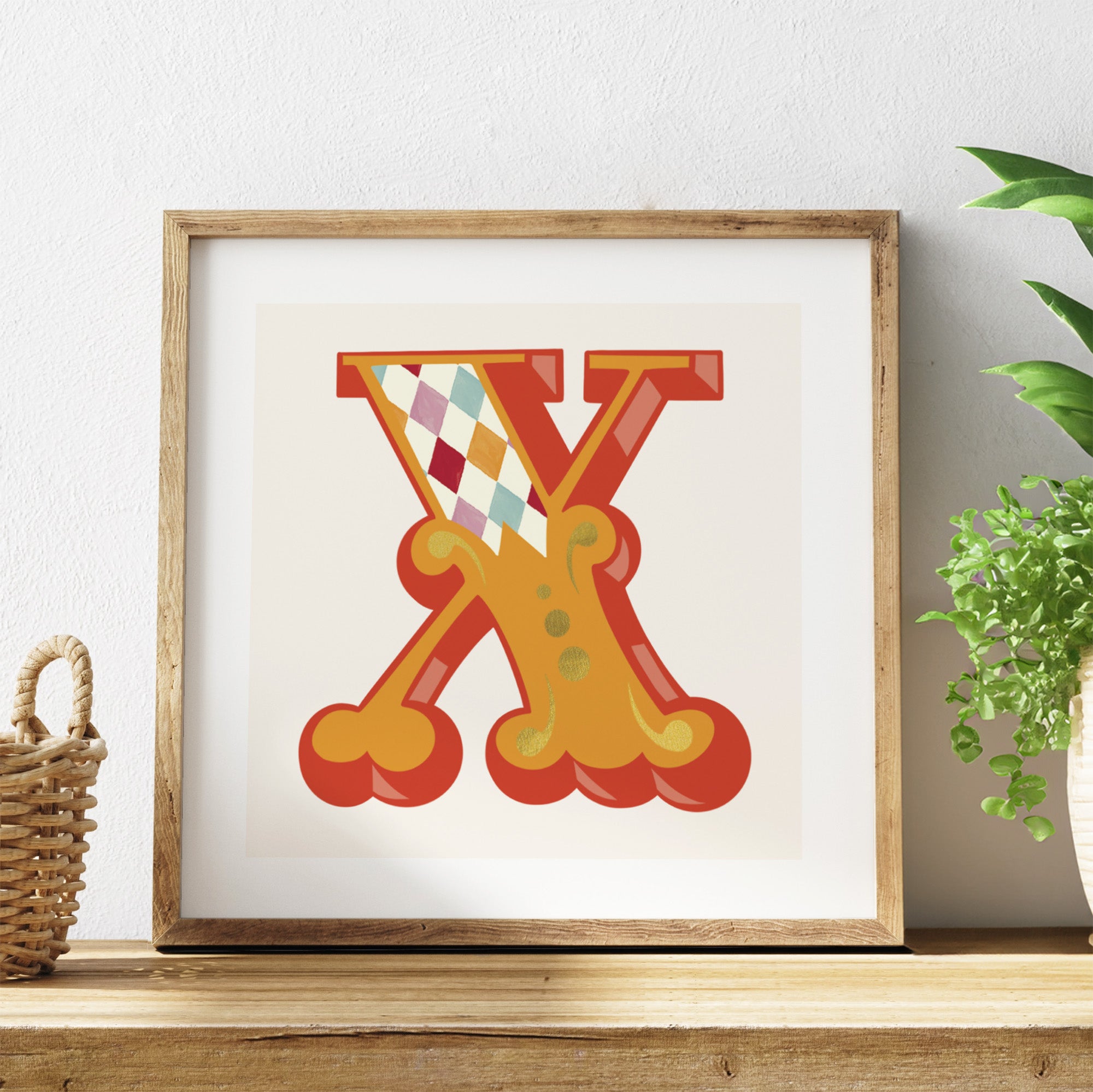 Framed artwork with a colourful letter 'X' on a white background, placed on a wooden surface with a plant in the corner.