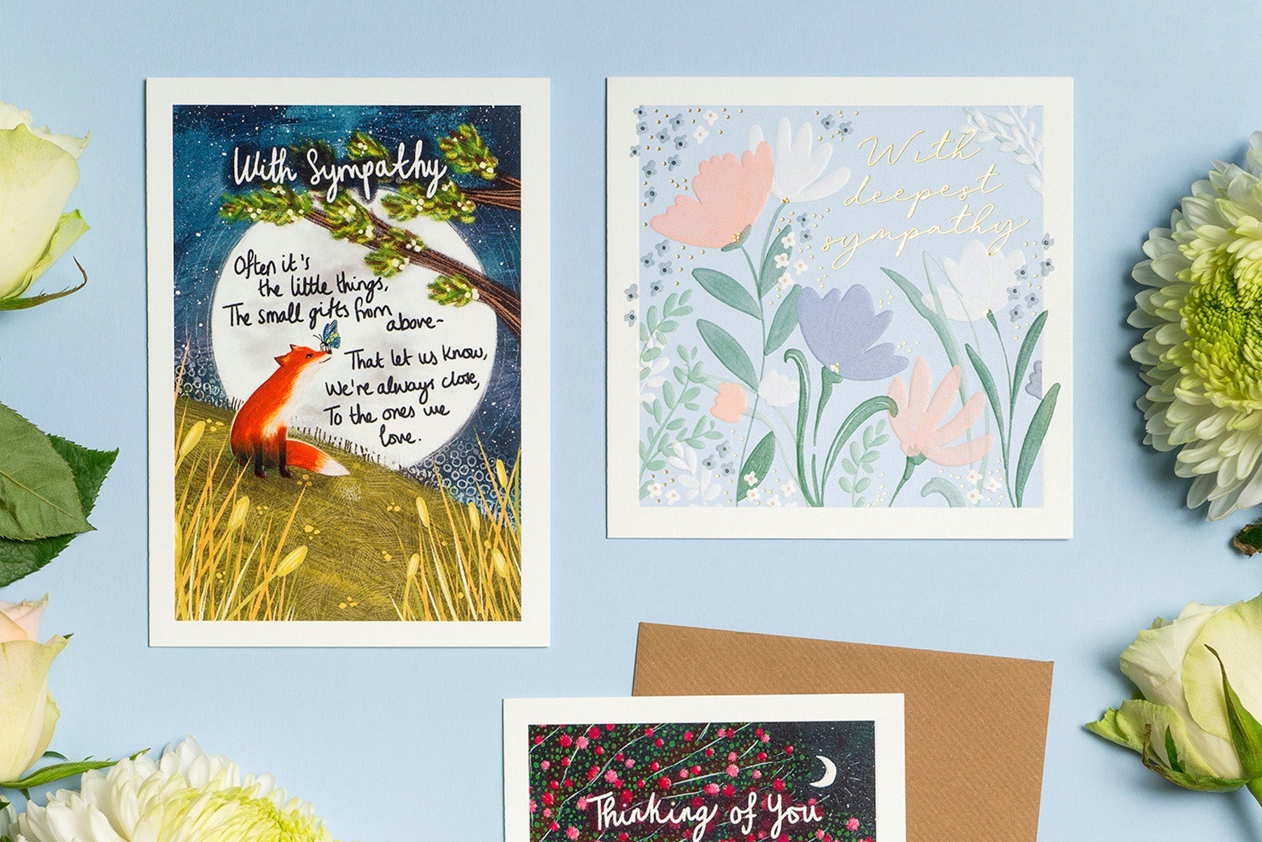 Thinking Of You cards laid out on a blue background with flowers.