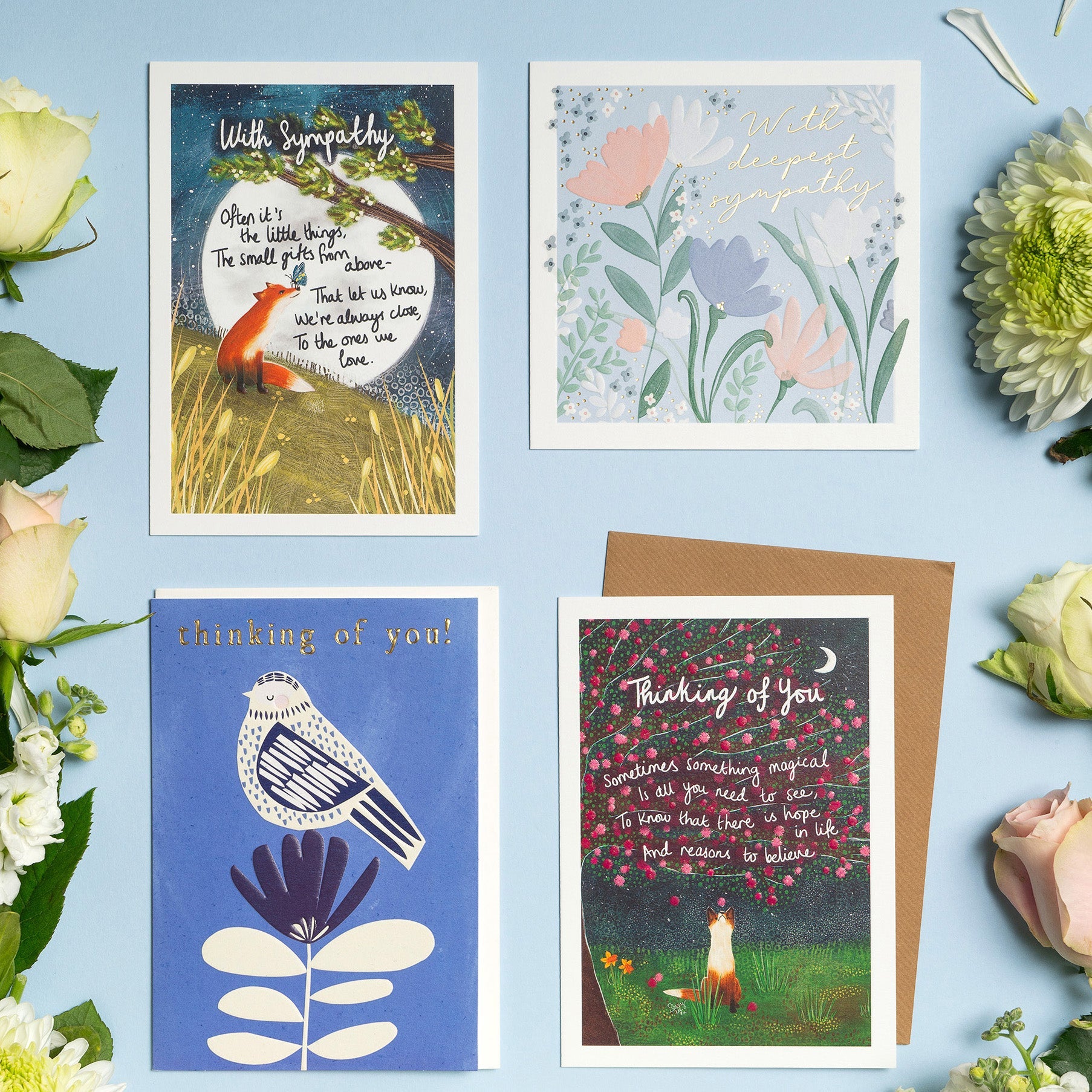 Thinking Of You cards laid out on a blue background with flowers.