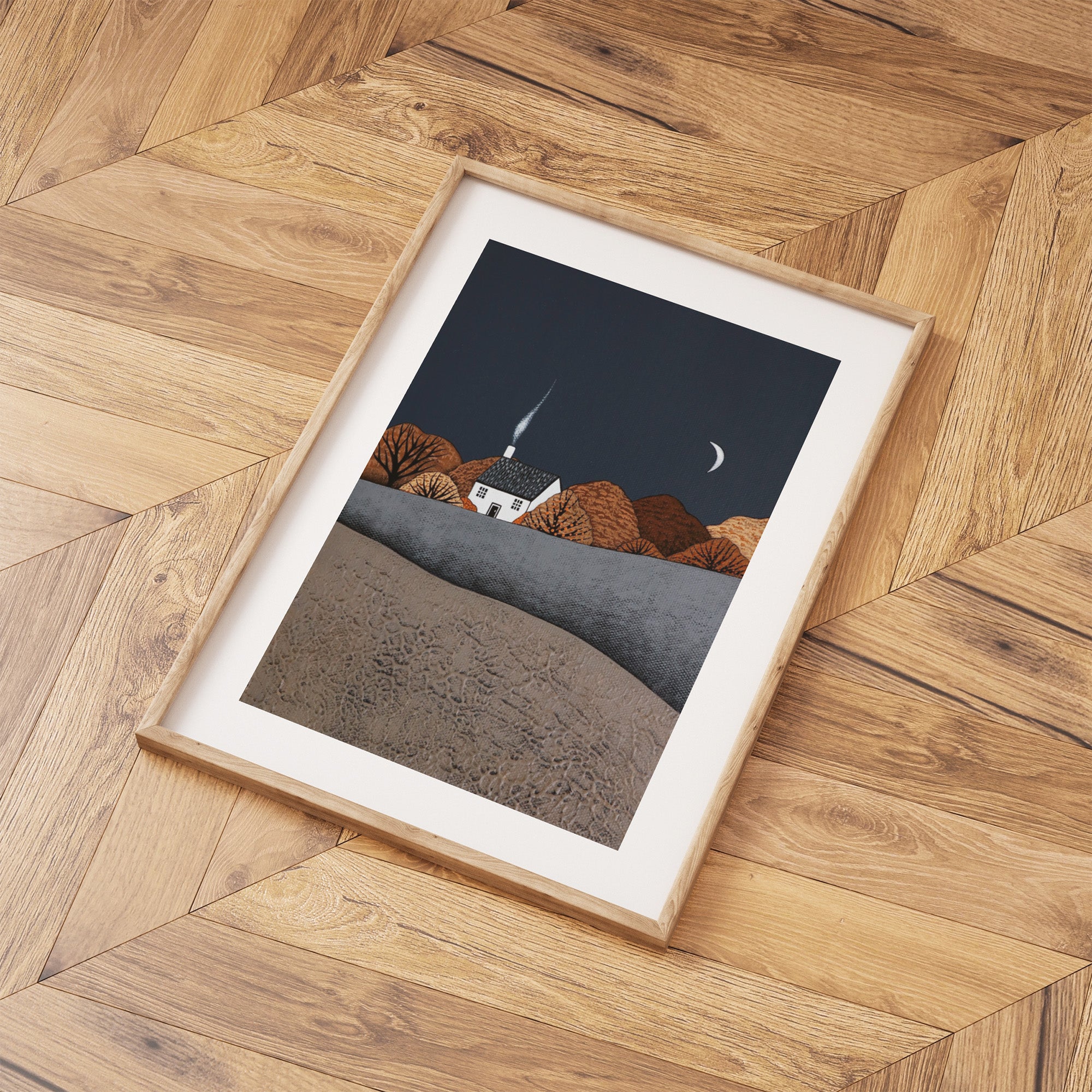 Framed artwork of an autumn landscape with a house, on a wooden floor.