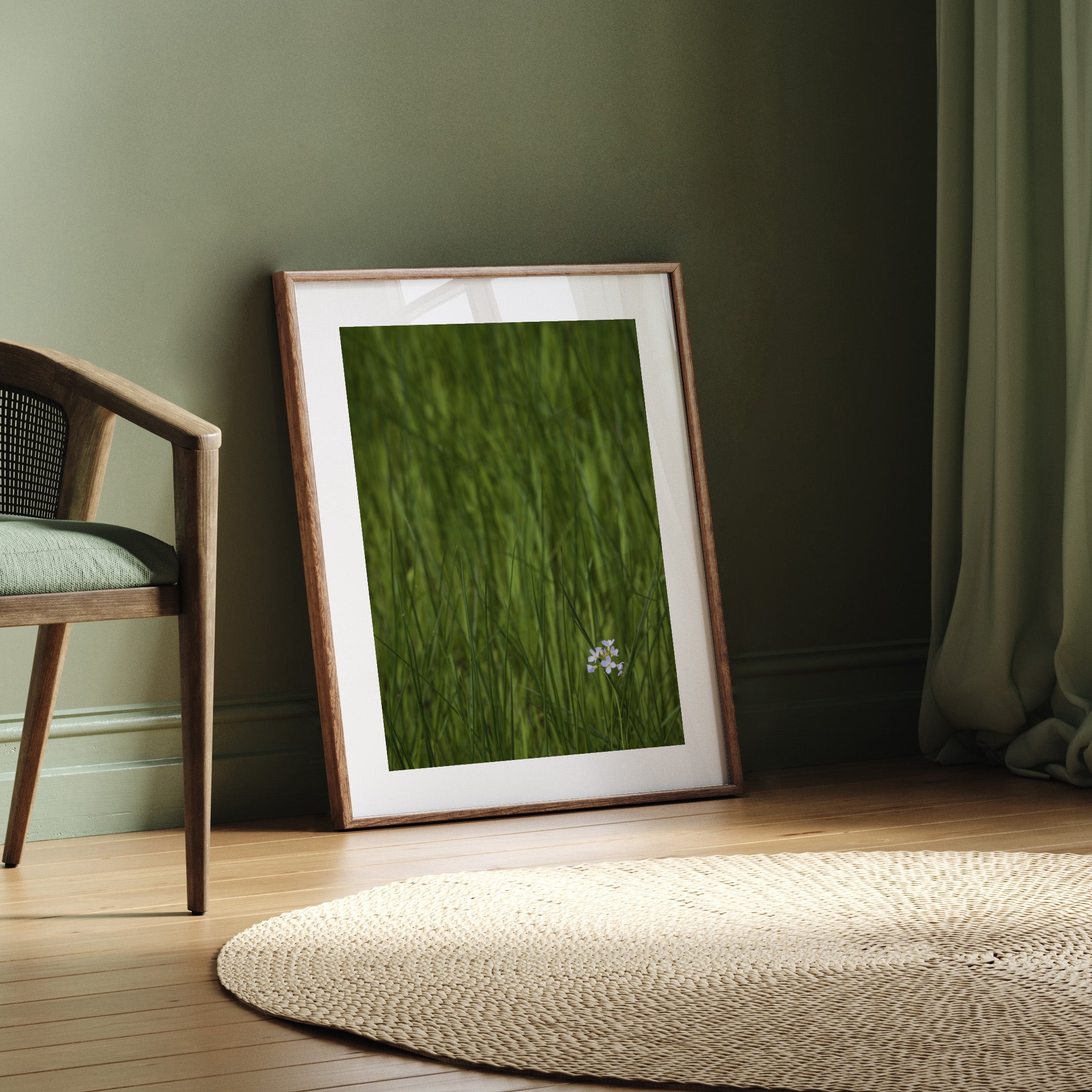 Beautiful framed photography art print featuring a vivid green field with a bright white flower nestled in the bottom corner. Framed print is leaning against a green wall.