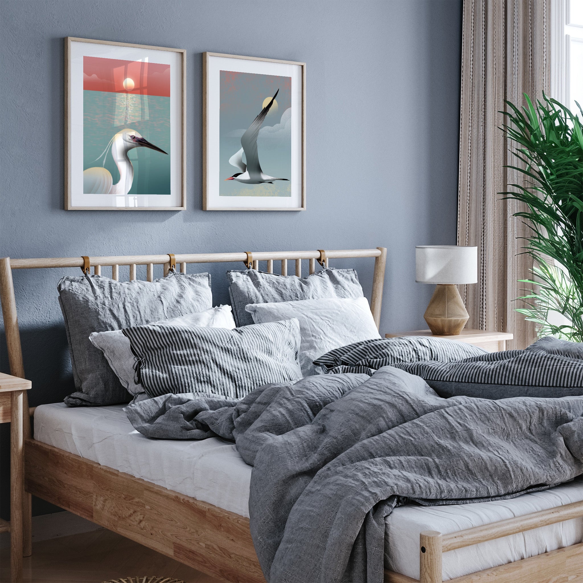 Framed art print featuring a white egret posing in from of the ocean, as the sun sets on the horizon. Another art print hangs next to it, both displayed in a bedroom.