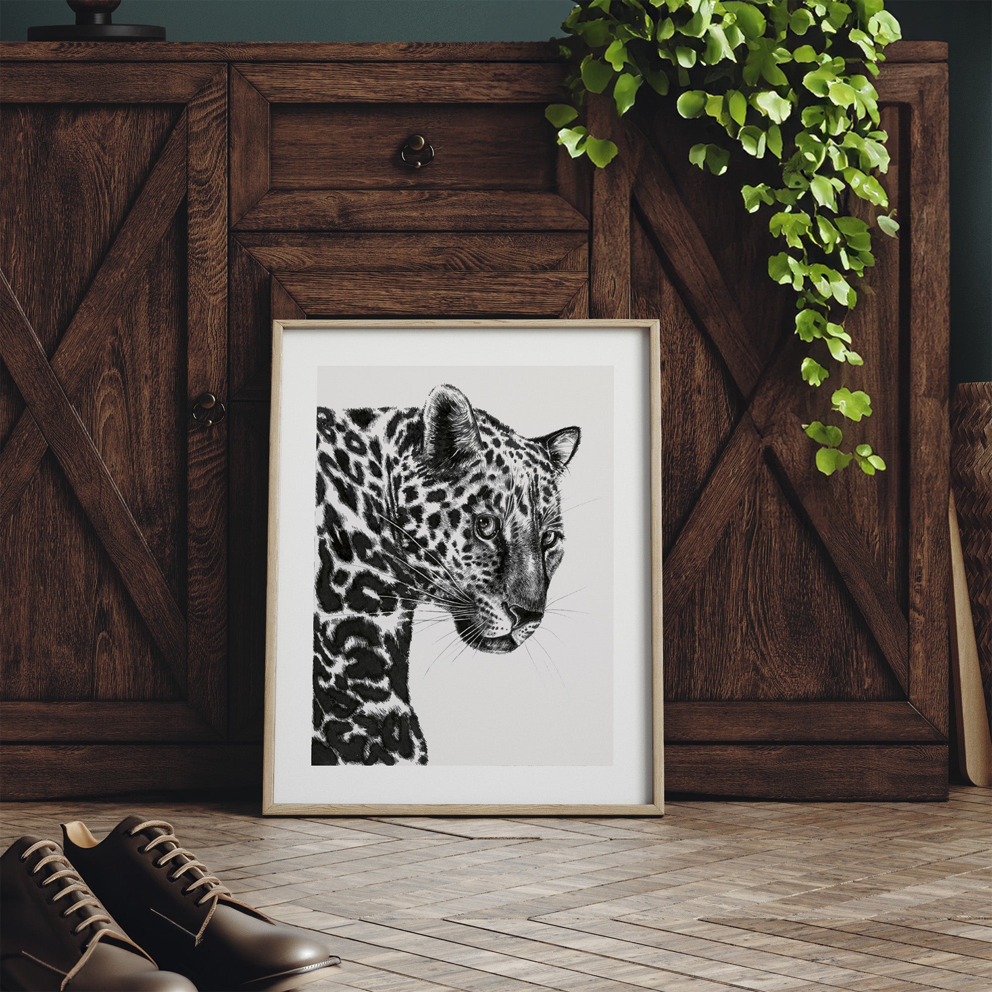 Framed art print featuring a detailed illustration of a leopard, in black and white. Print is leaning against a dresser.