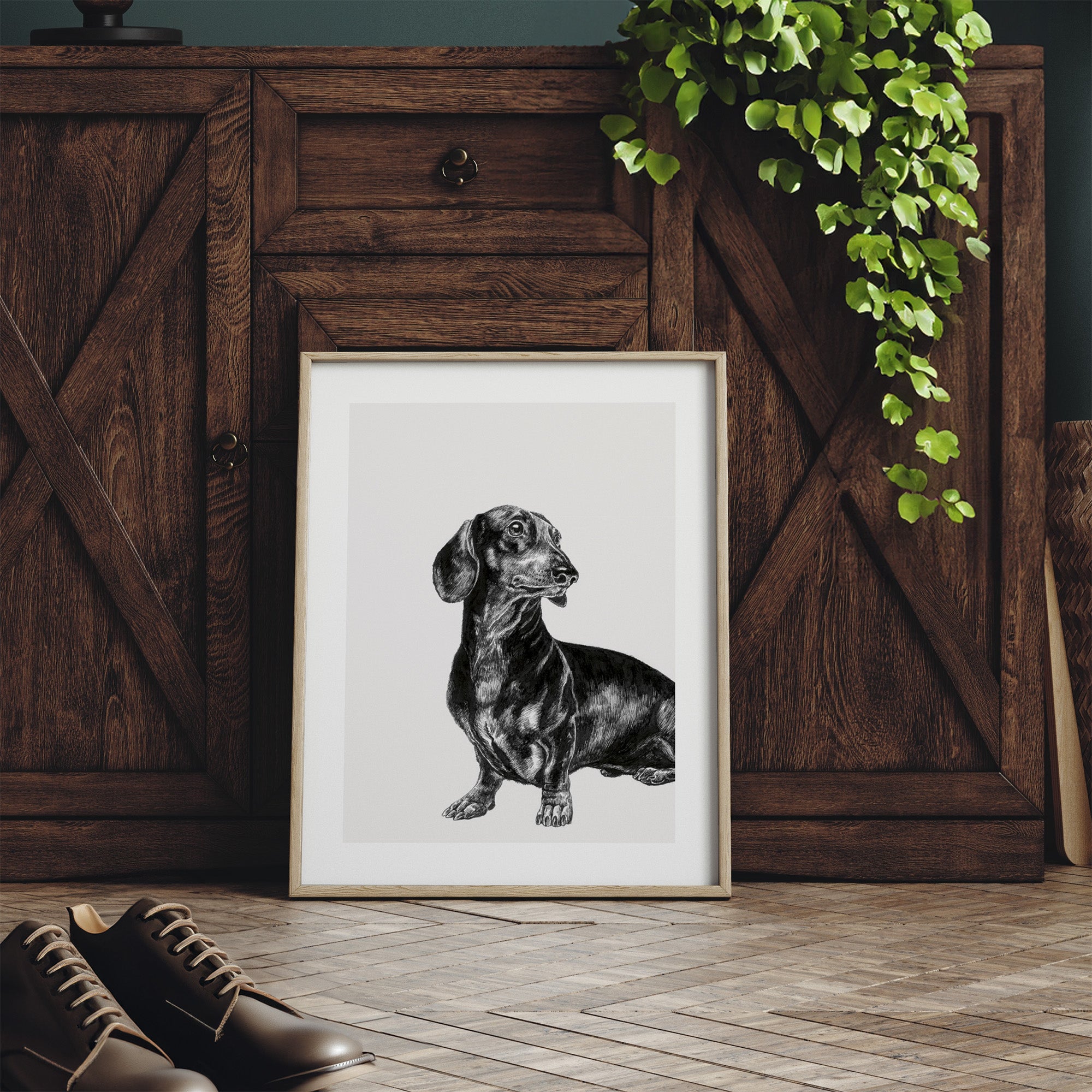 Framed black and white illustration featuring a detailed drawing of a Dachshund dog. Print is leaning against a dresser.