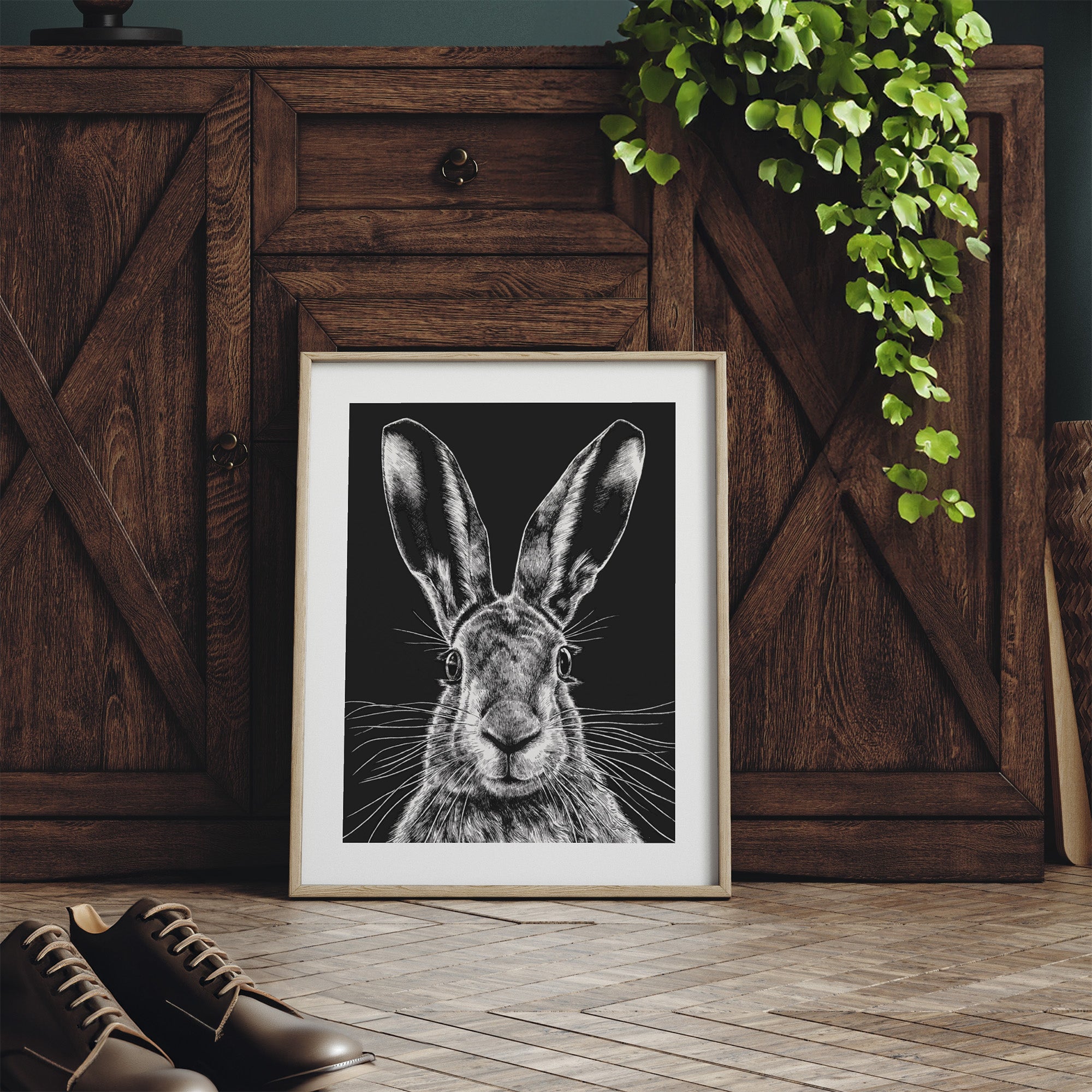 Framed art print featuring a detailed illustration of a wild hare, in black and white. Print is leaning against a dresser.