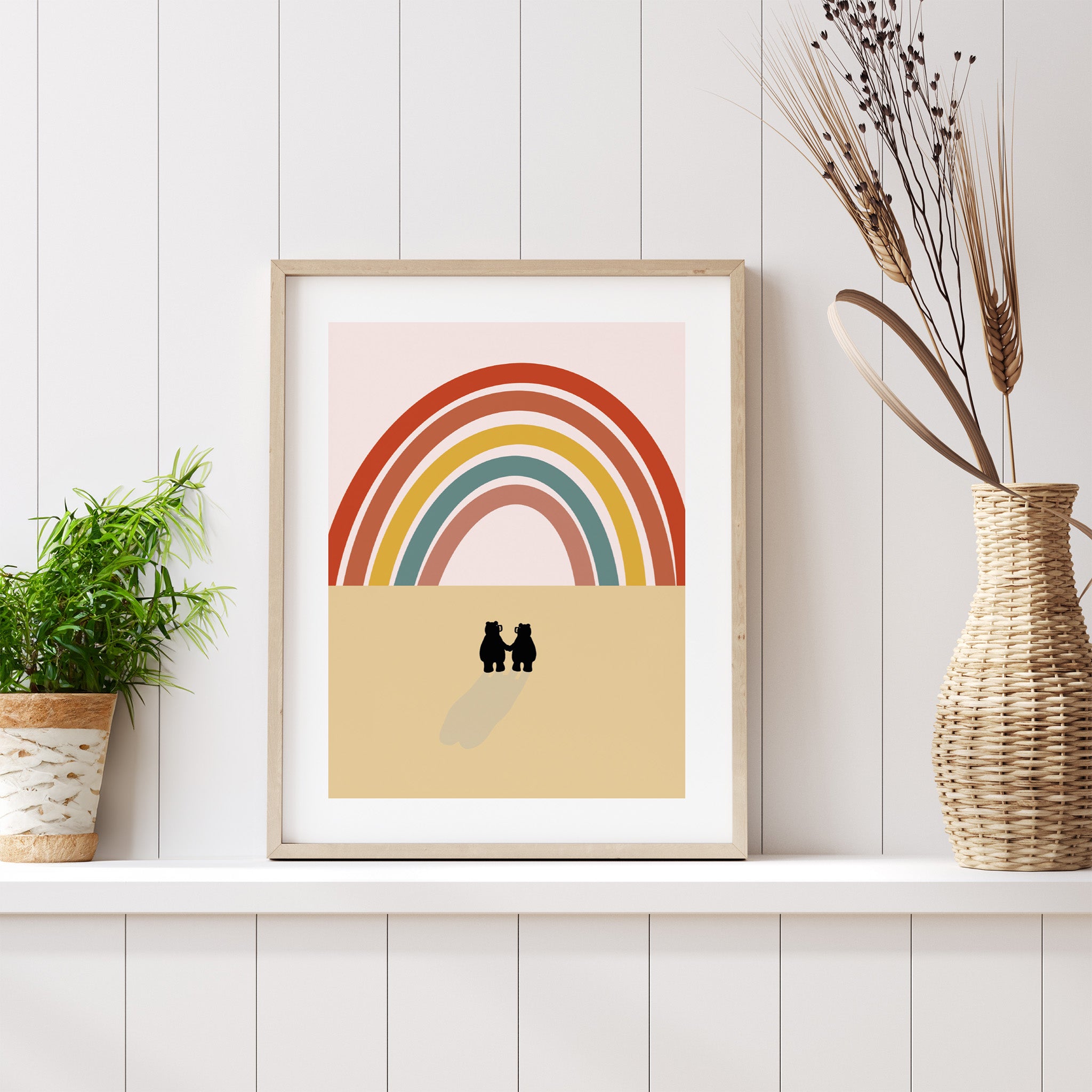 Framed artwork with a rainbow and two figures on a beige background, placed on a white shelf with decorative elements.